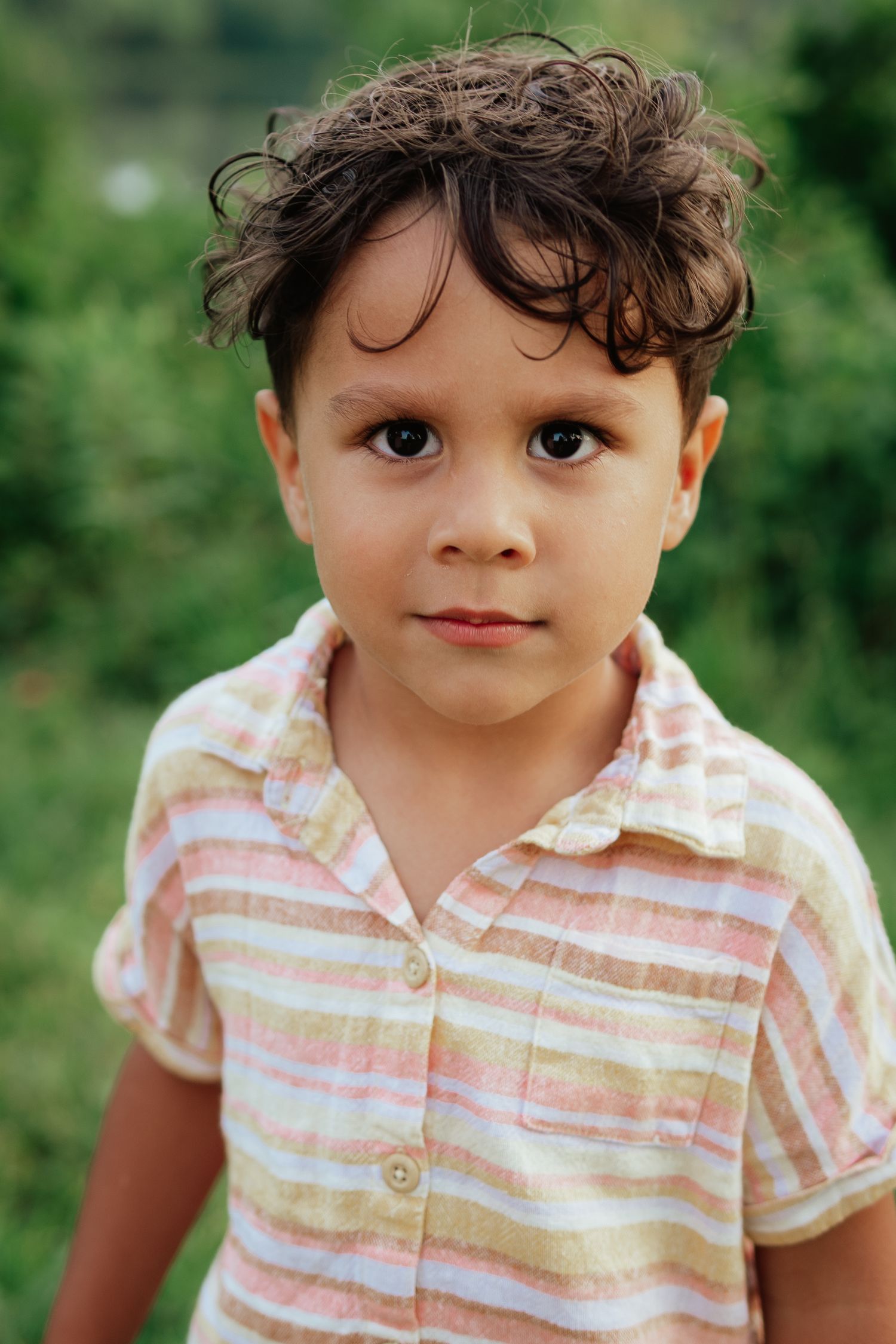 A child in a pink and white striped collared shirt is shown in a series of four headshot photos outdoors.
