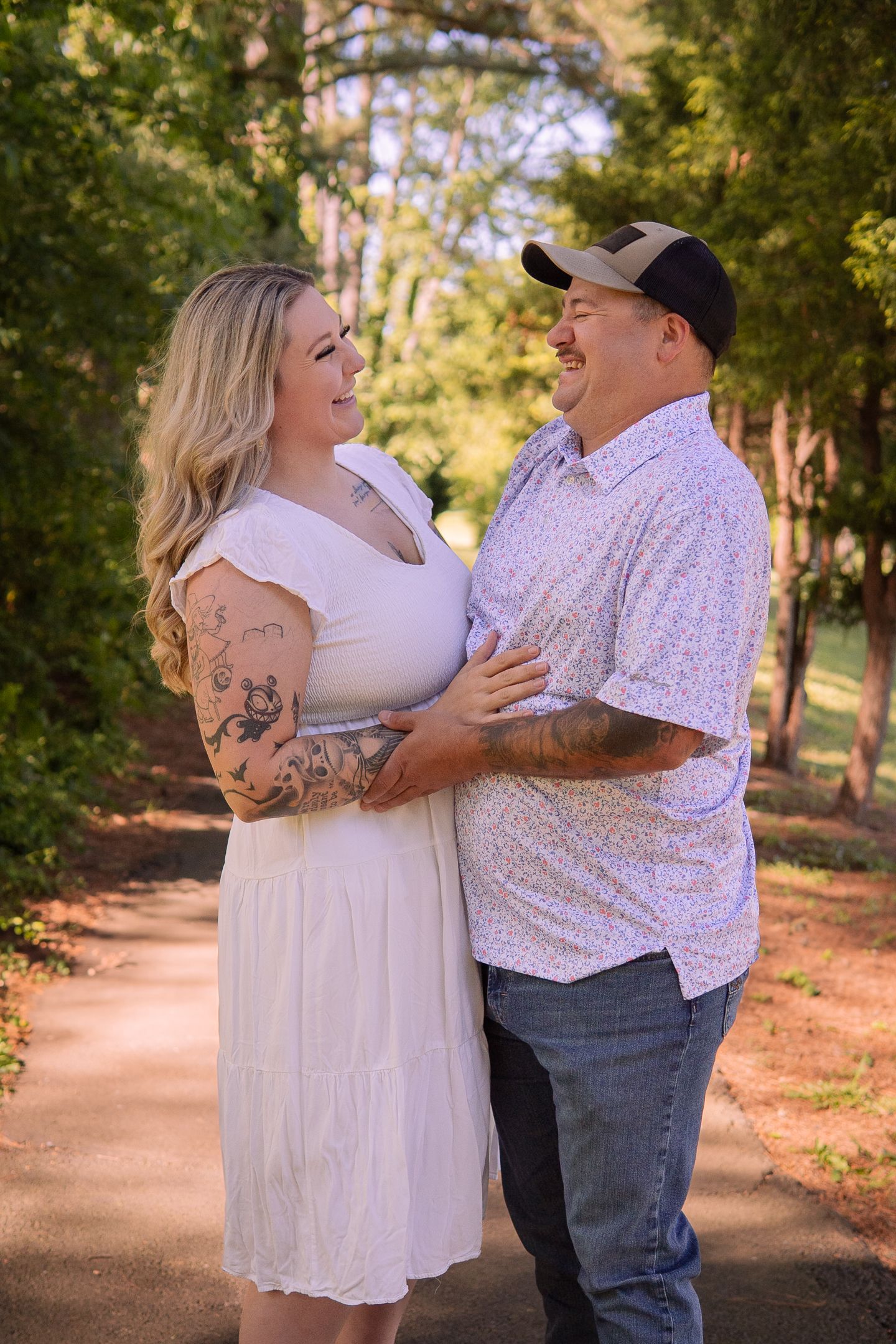 Romantic couple embracing outdoors on a tree-lined path during a sunny afternoon.