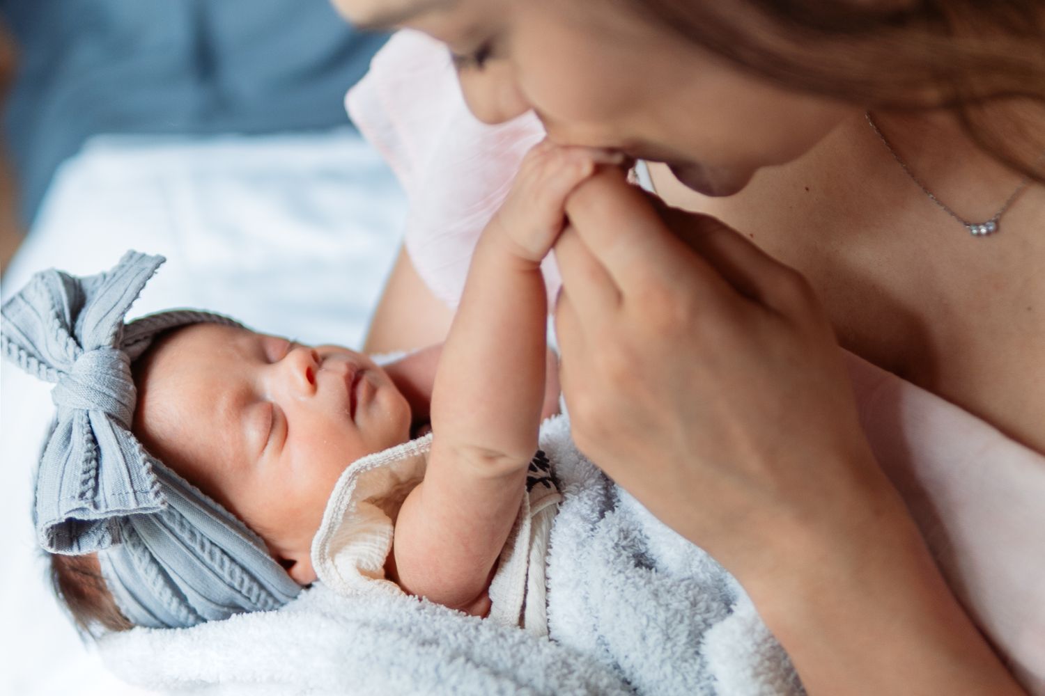 A tiny newborn baby sleeping peacefully in soft white bedding while swaddled in a light blue blanket.