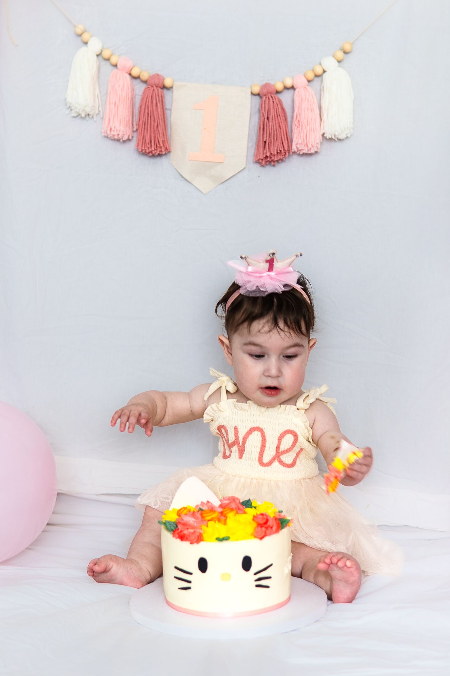 Birthday scene with pink tassel garland and Hello Kitty cake decorated with colorful flowers.