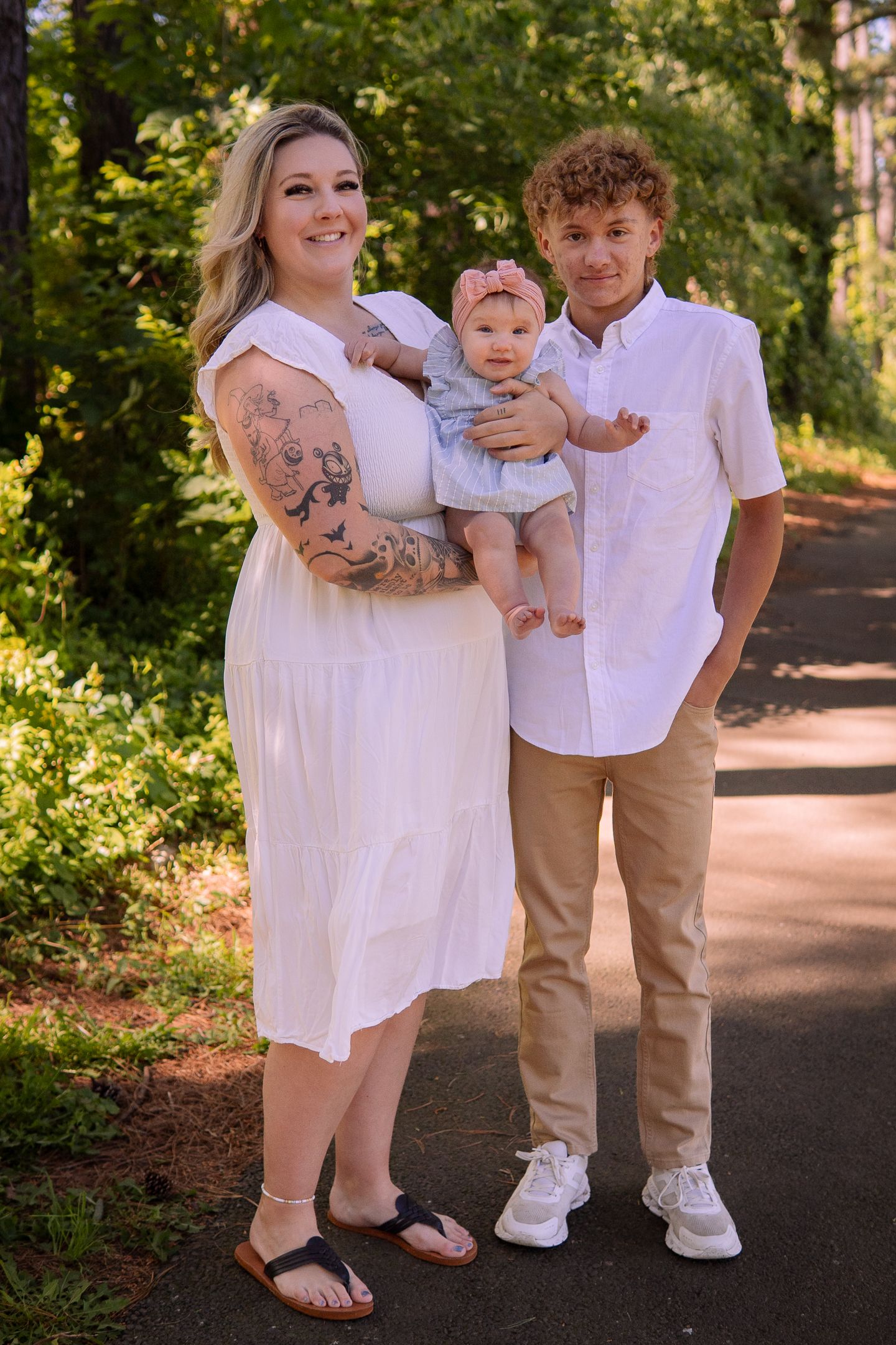 Three family members pose on a wooded path wearing coordinated white and neutral outfits.