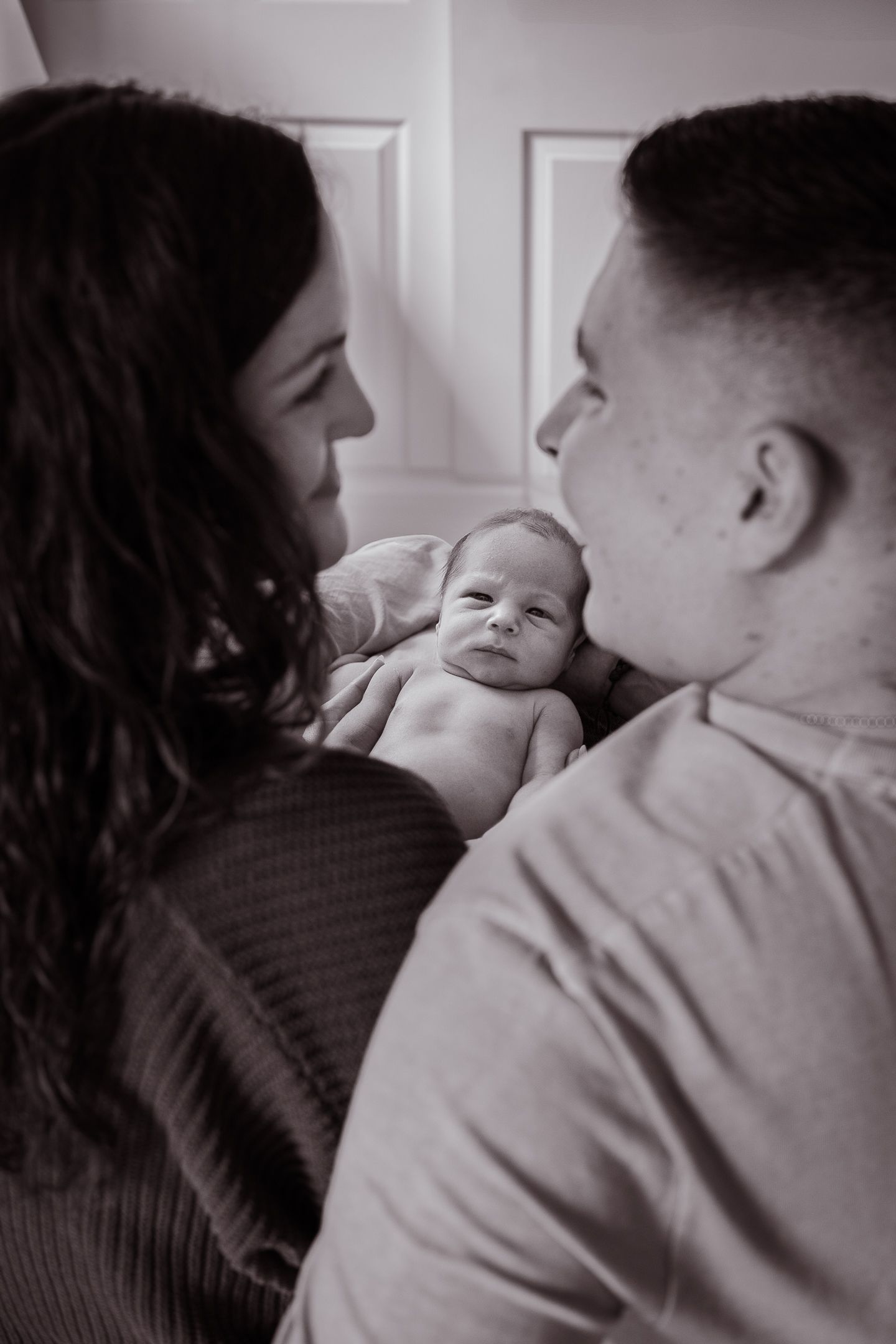 Intimate black and white portrait of new parents gazing at their newborn baby.