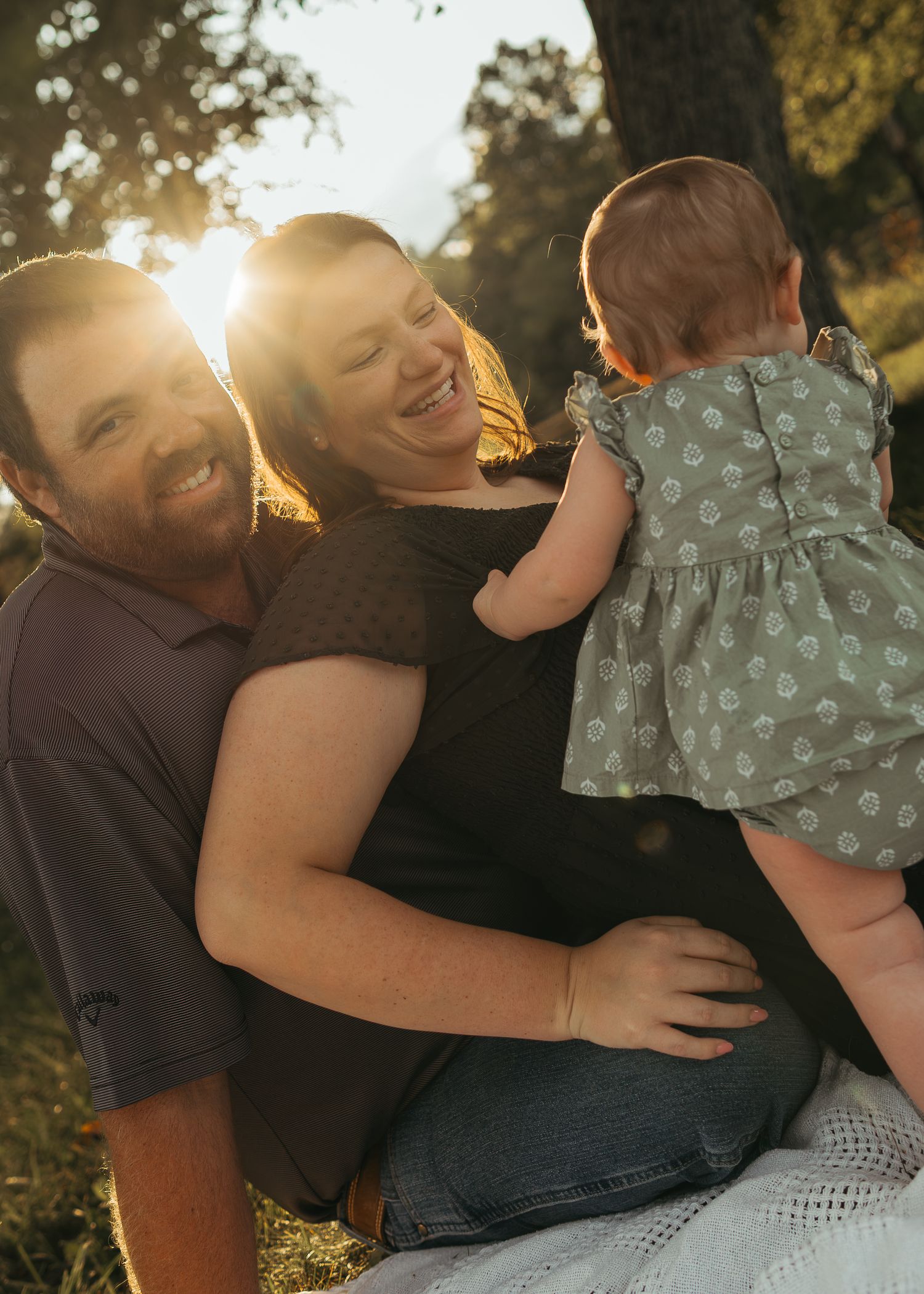 Happy couple laughing with baby girl during golden sunset maternity family photography session outdoors.
