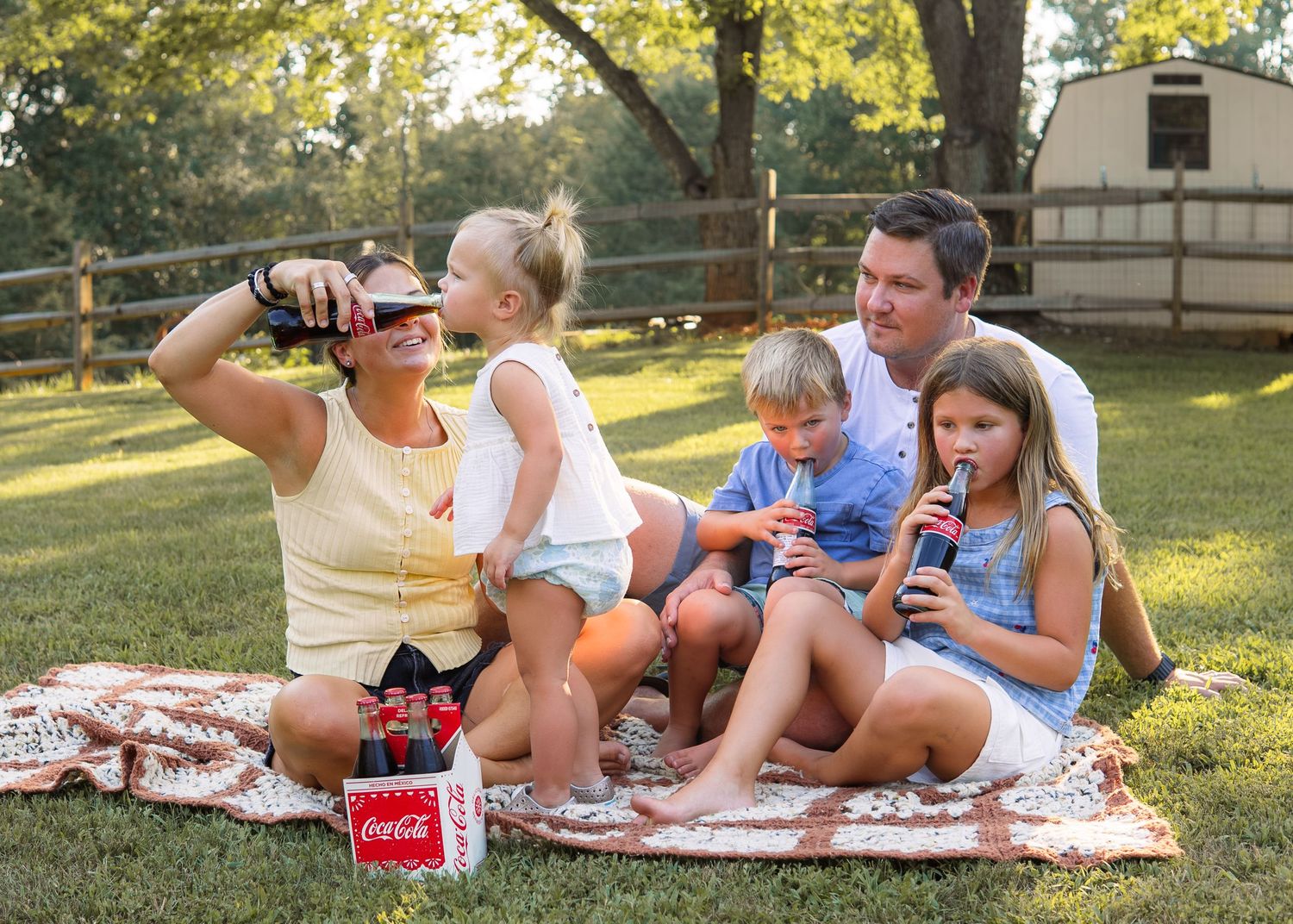 Family enjoying Coca-Cola drinks on a picnic blanket in a sunny backyard.