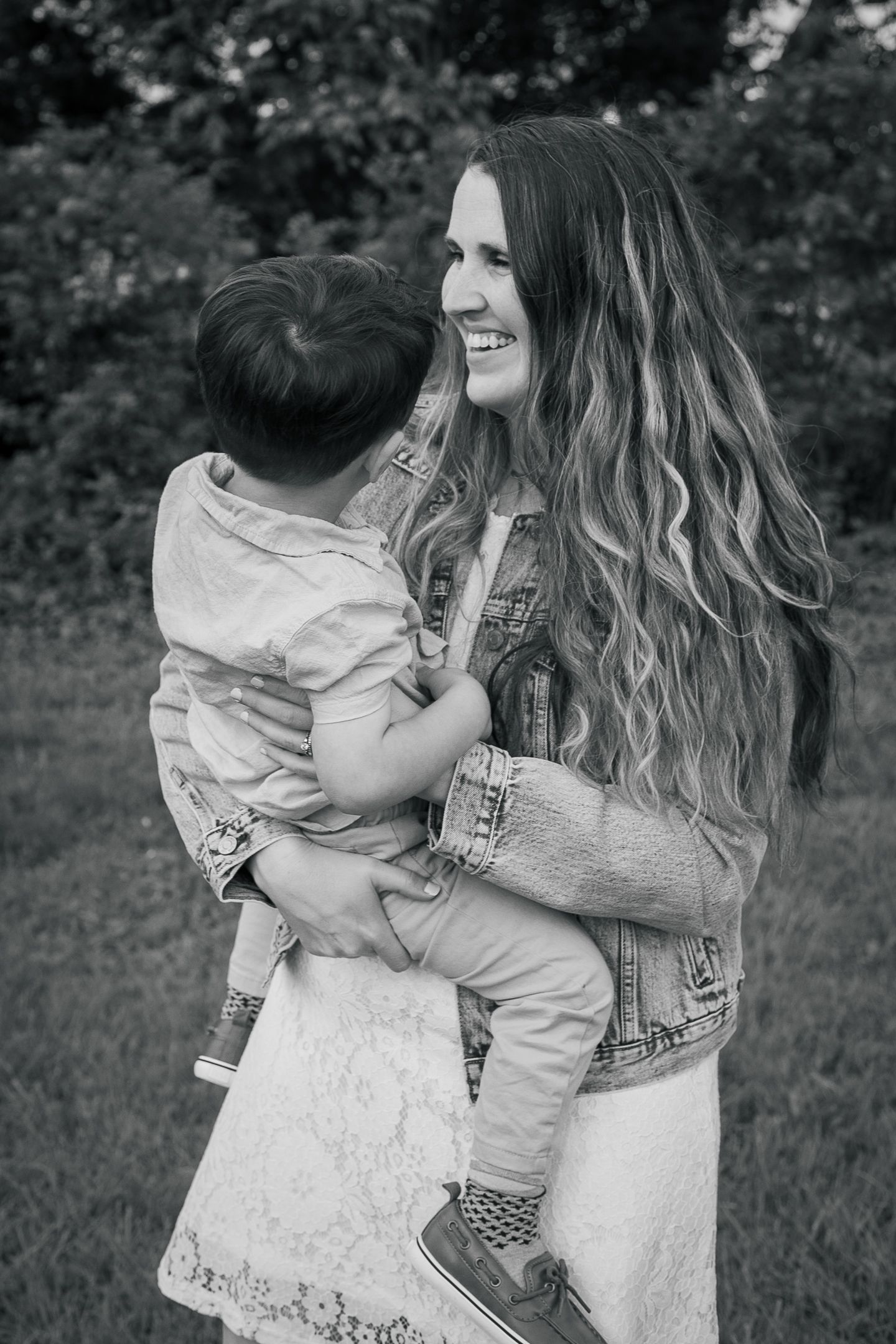 Black and white outdoor portrait of a nurturing parent holding and smiling at a small child in casual denim attire.