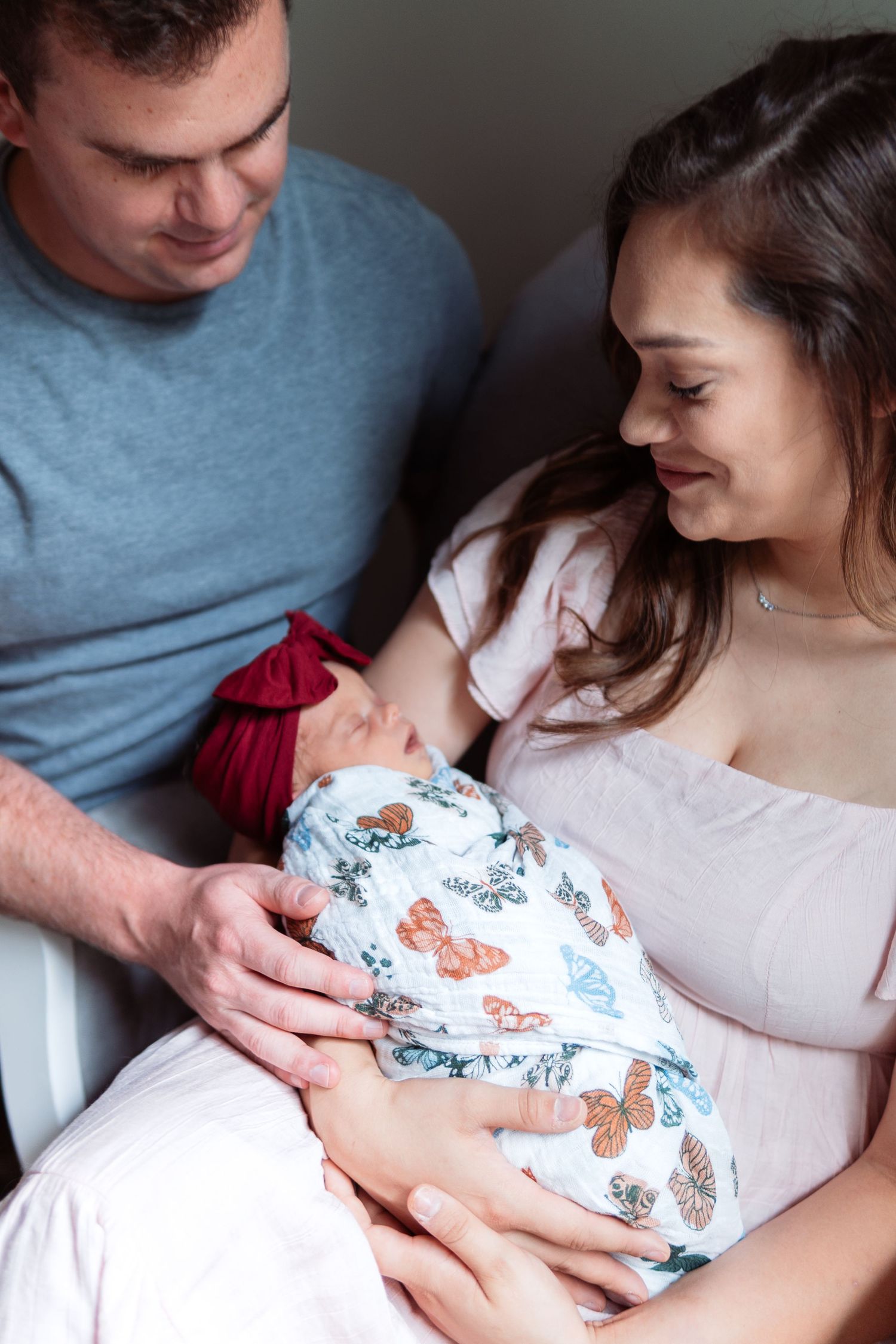 An intimate portrait of new parents cradling their baby wrapped in a butterfly patterned swaddle.