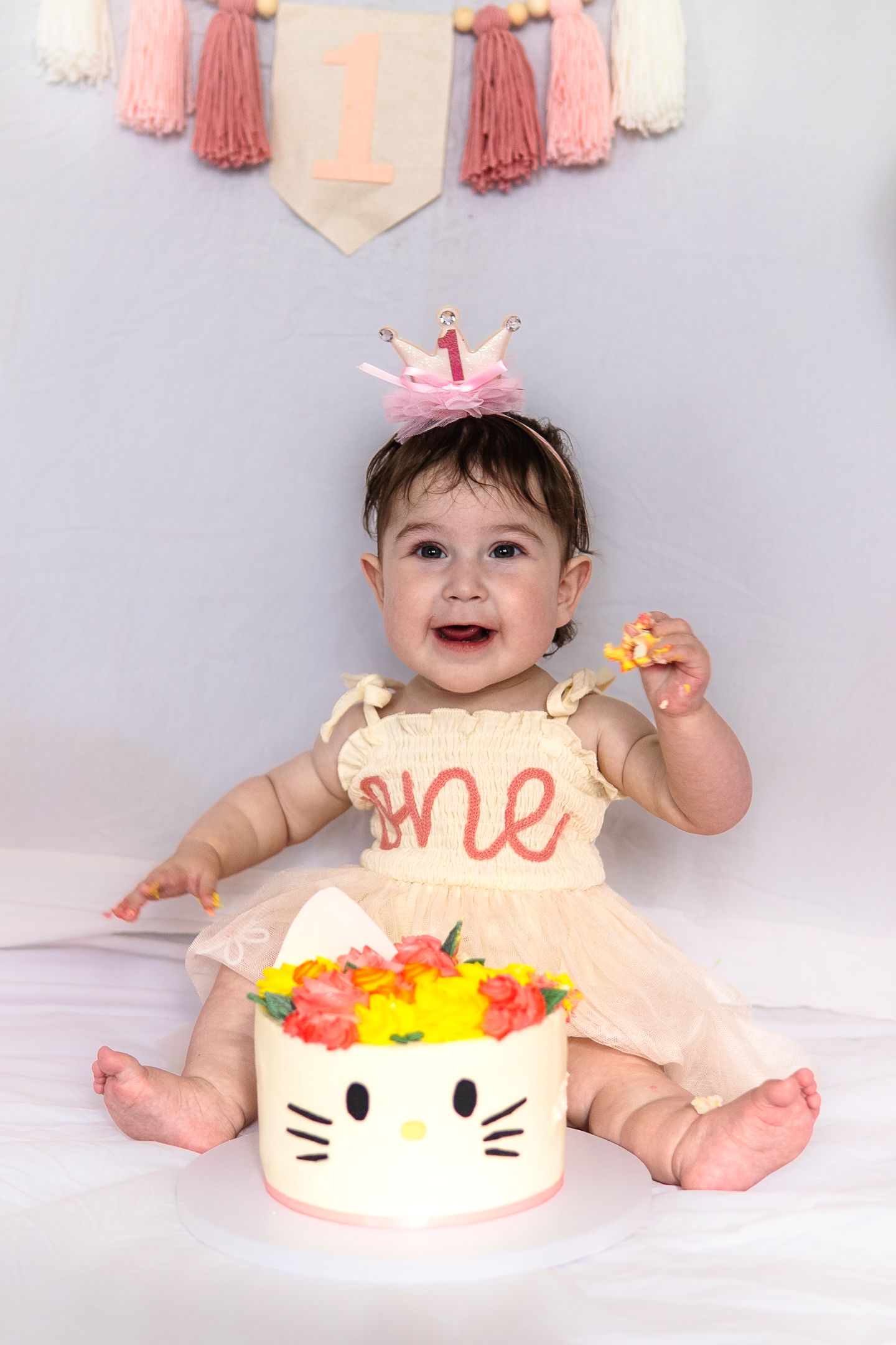 First birthday celebration with Hello Kitty cake and pink decorations including tassel banner and pink crown.