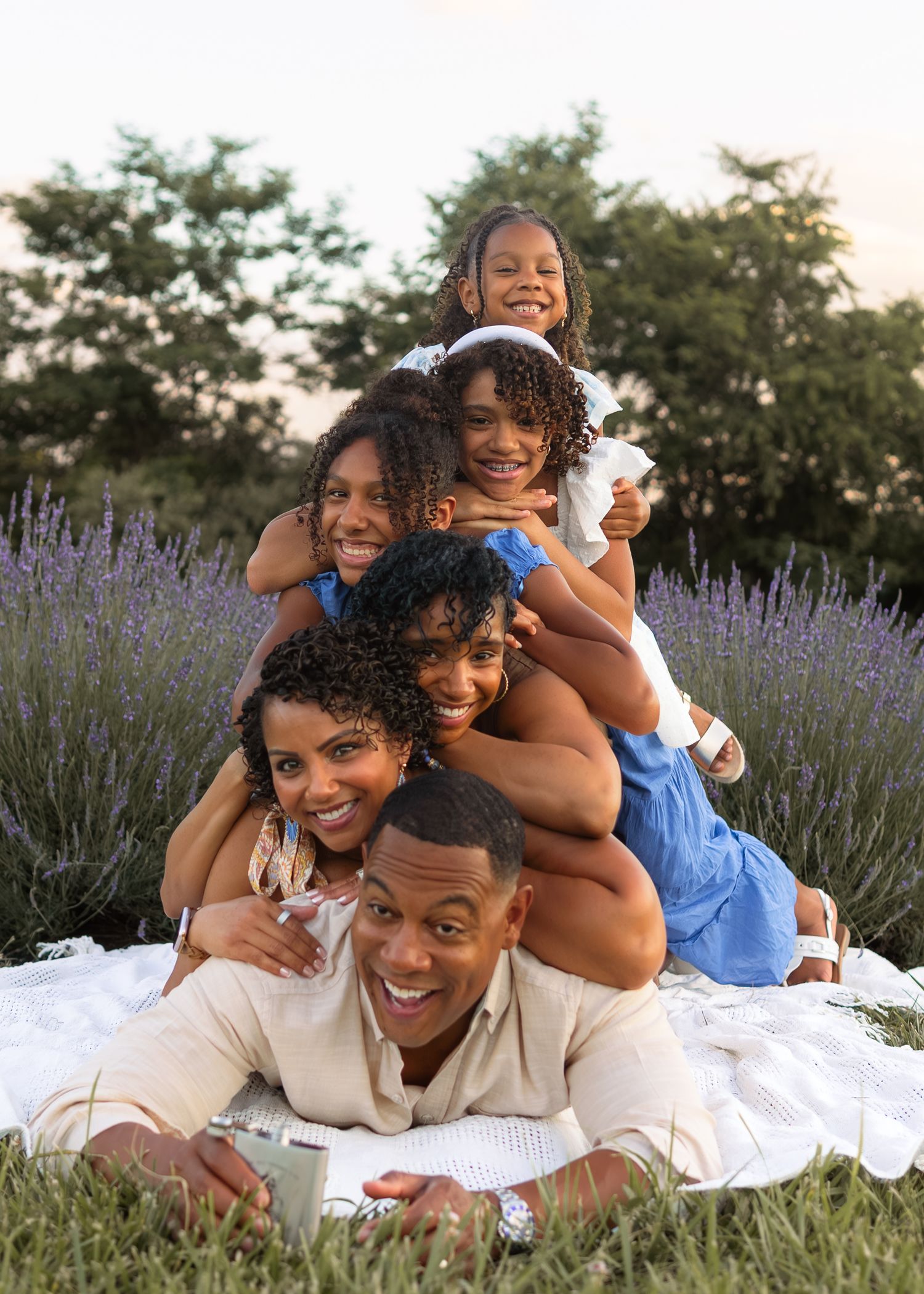 Happy Black family of five posing in a lavender field, stacked in a playful pyramid on a white blanket.