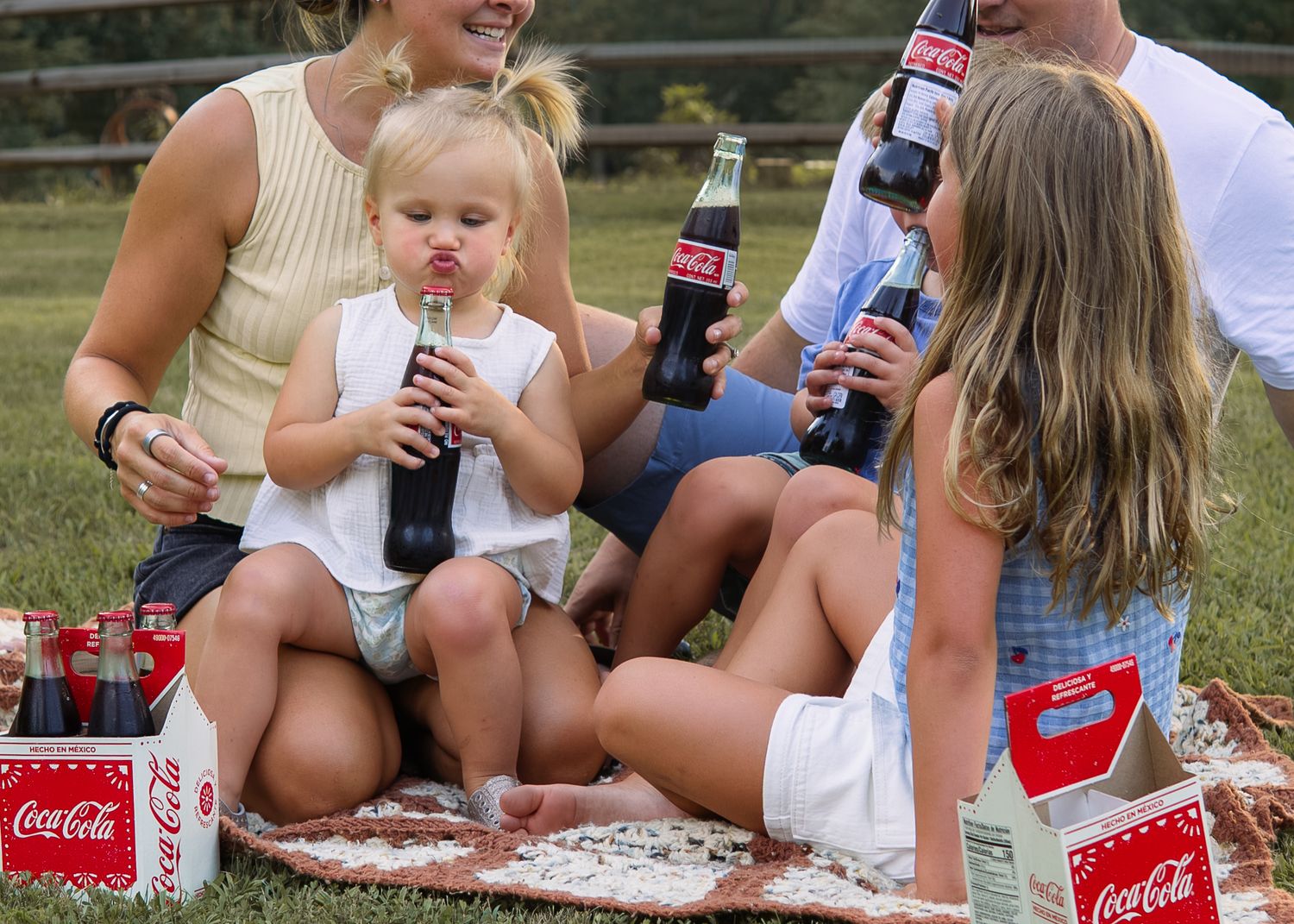 Family enjoying Coca-Cola bottles at an outdoor picnic on a blanket with Coca-Cola boxes nearby.