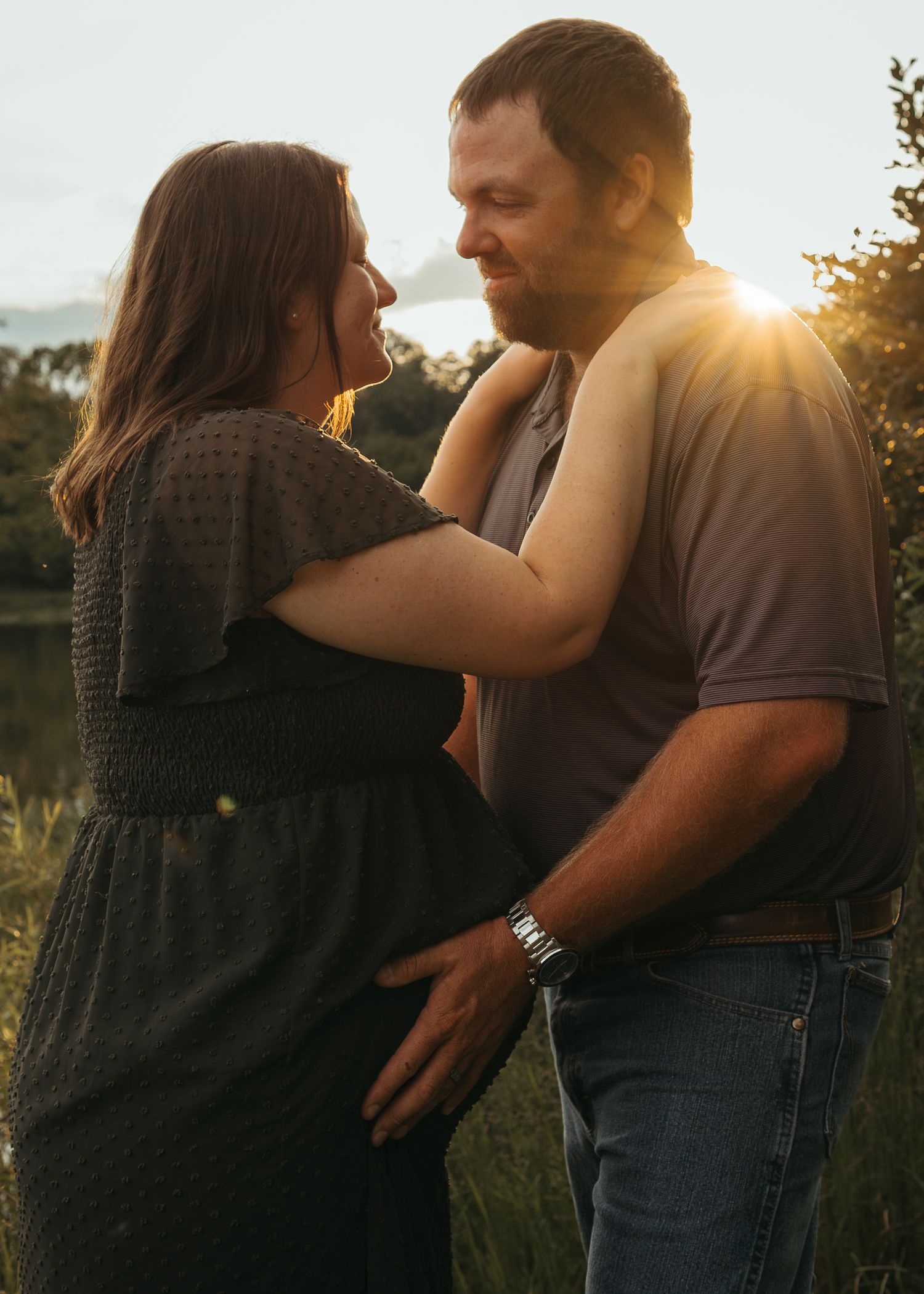 Couple sharing a romantic moment outdoors at golden hour sunset, woman in black dress with man in gray shirt and jeans.
