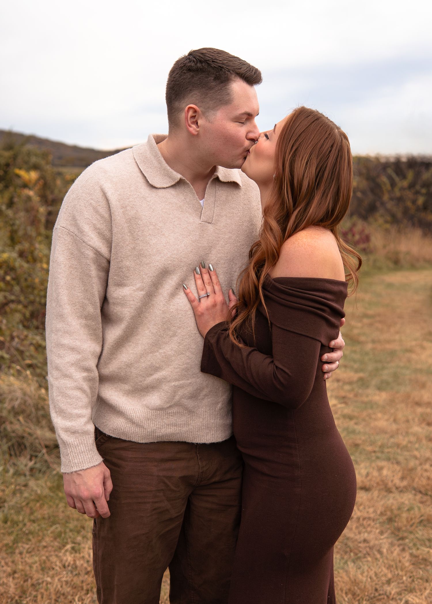 Couple sharing a romantic kiss outdoors in a field during an engagement photo session.