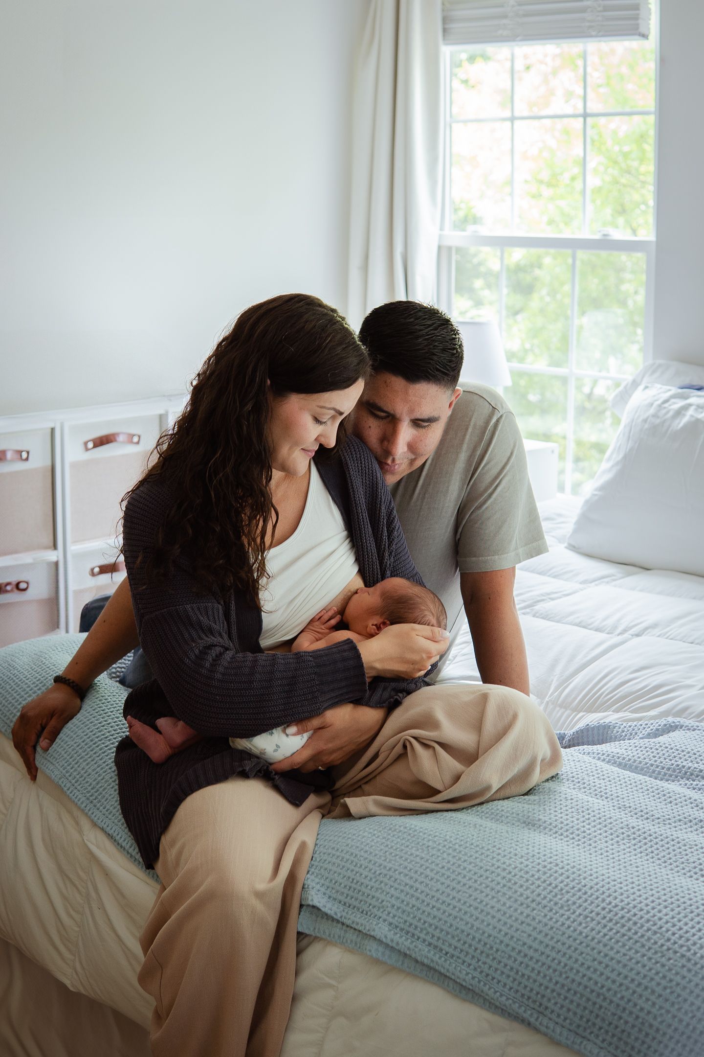 Parents sitting on bed together tenderly holding and looking at their newborn.