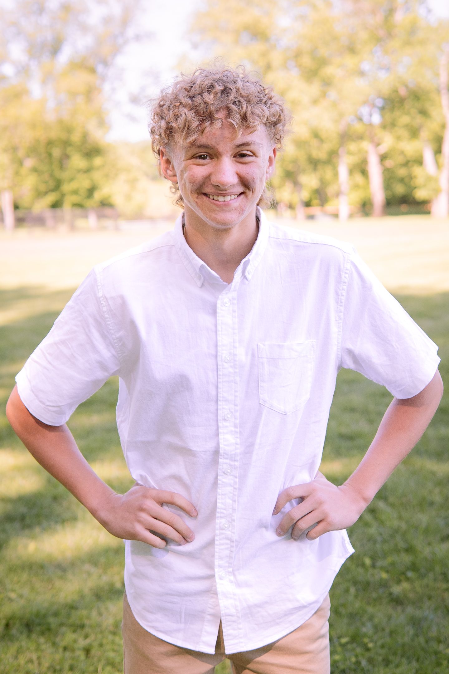 Young person in crisp white button-down shirt poses confidently outdoors with hands on hips.