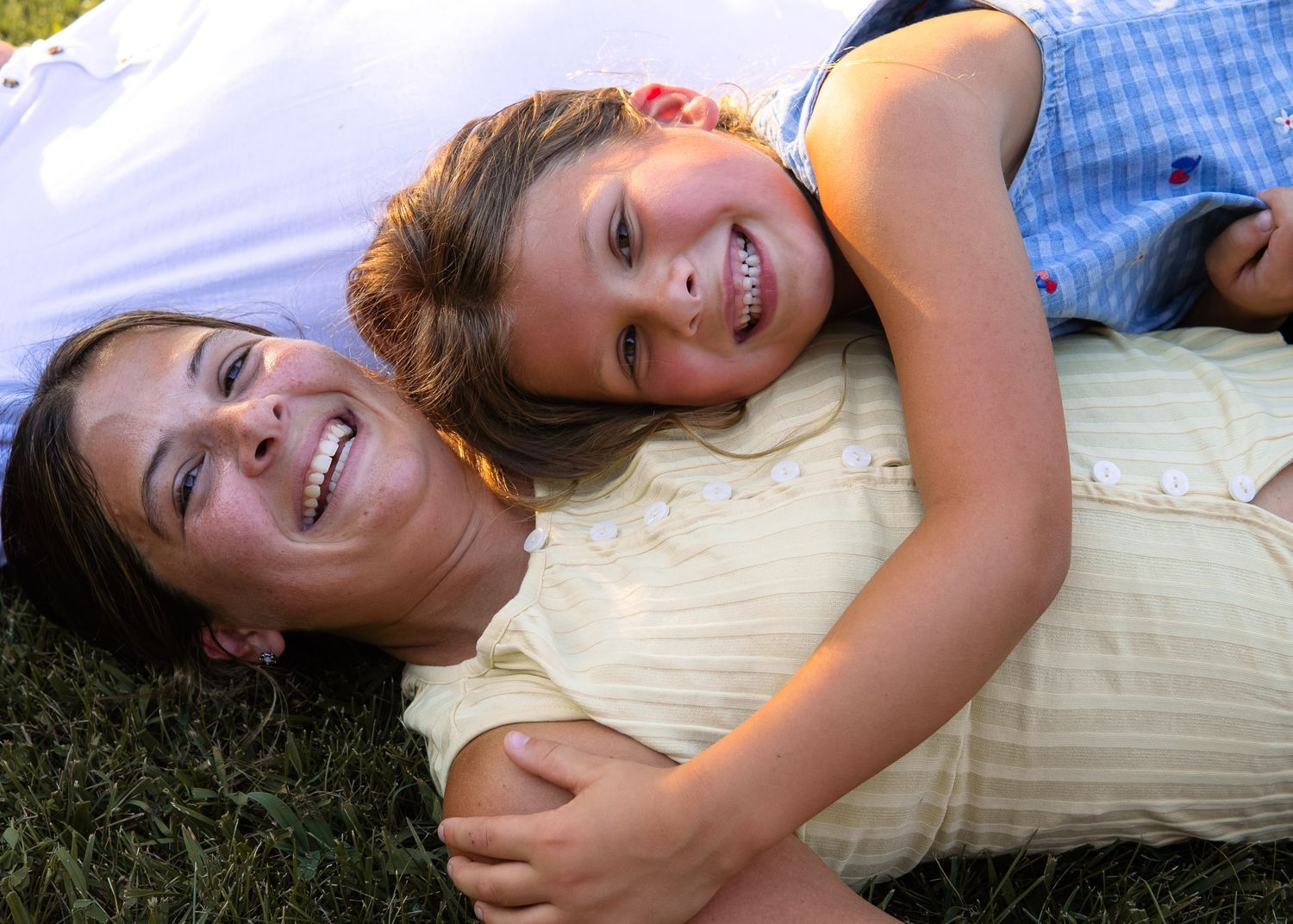 Mother and daughter laughing together while lying on green grass.