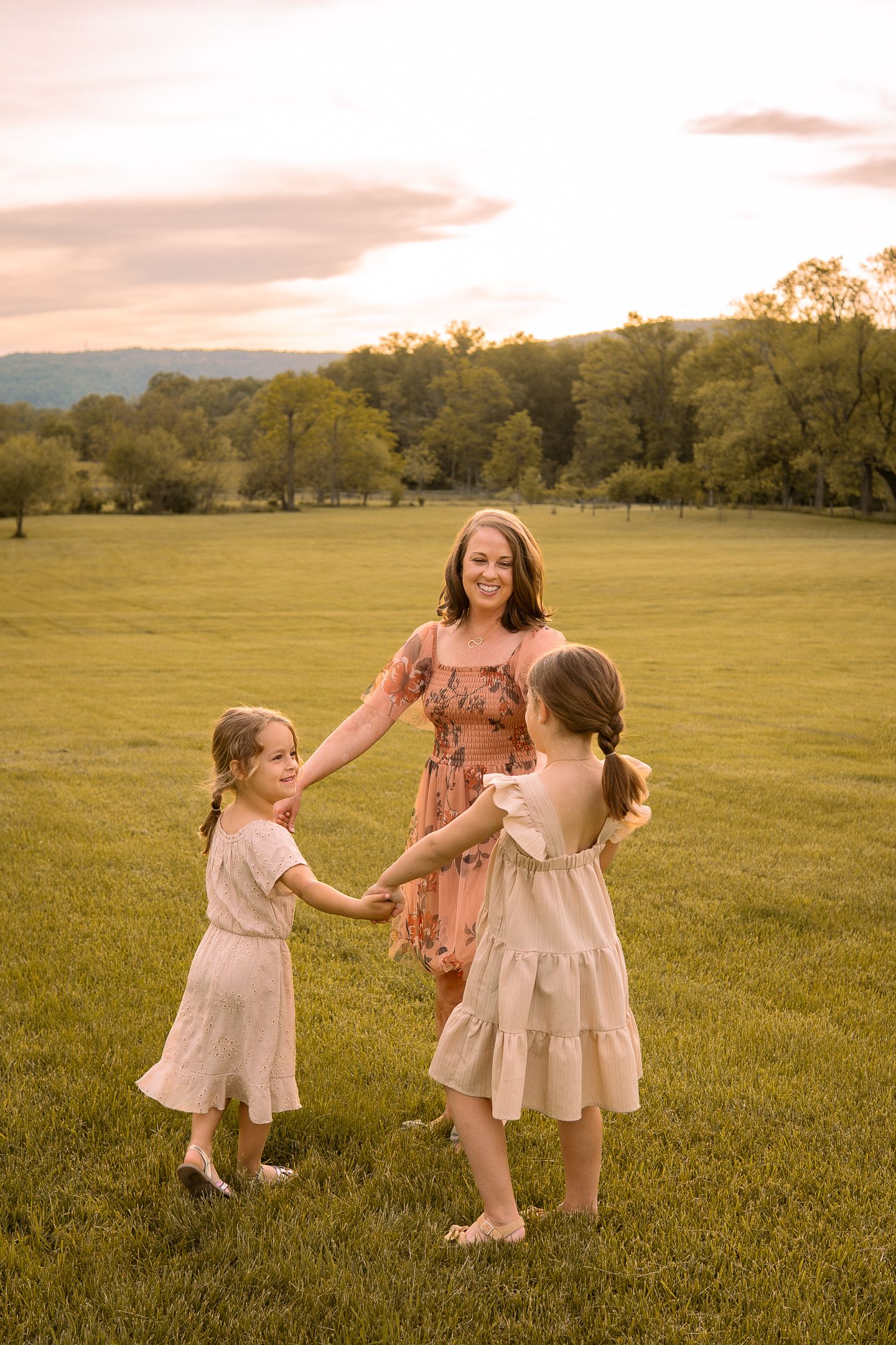 Three people play together joyfully on a golden sunlit meadow during sunset.