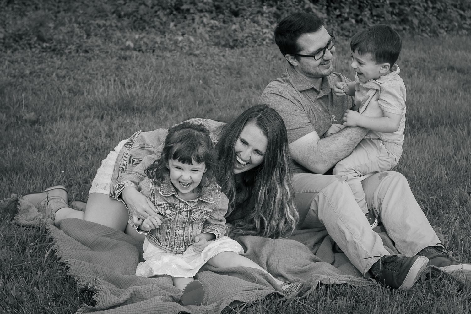 A family relaxes together on a blanket outdoors, enjoying a casual picnic on the grass.