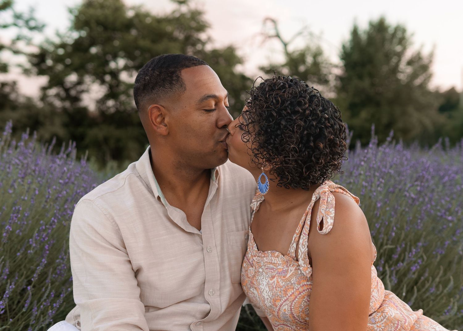 Romantic couple sharing a kiss while sitting in a blooming lavender field at sunset.