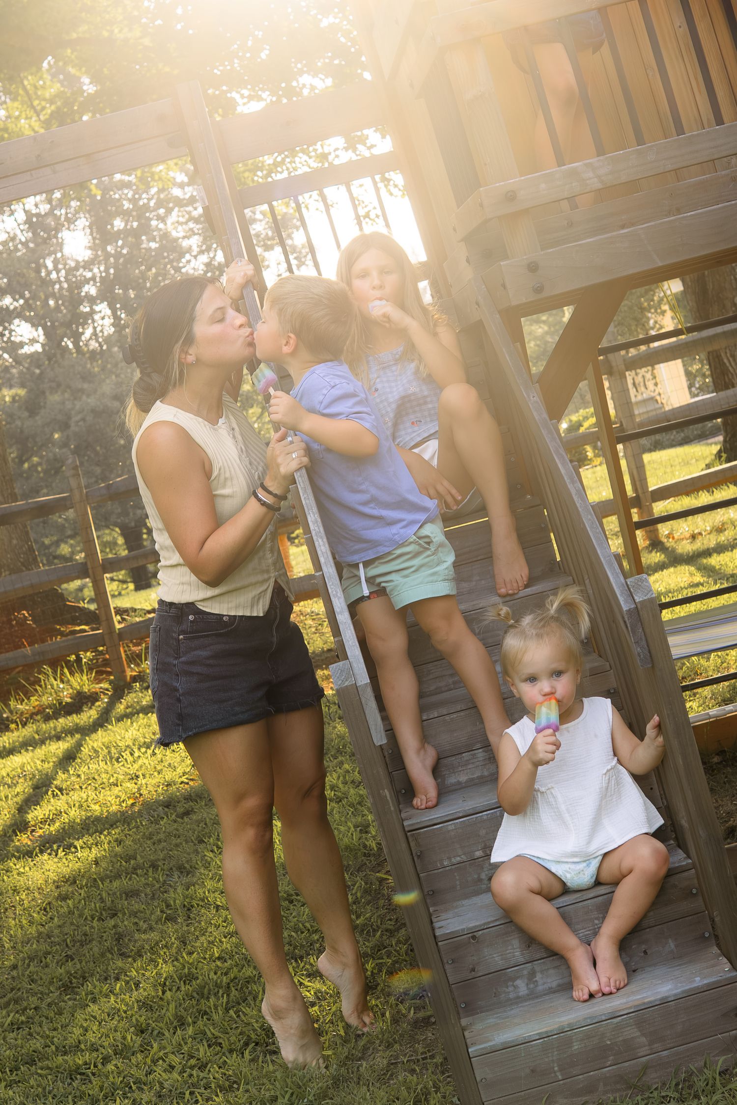 Children enjoying popsicles on wooden playground steps in sunny backyard.