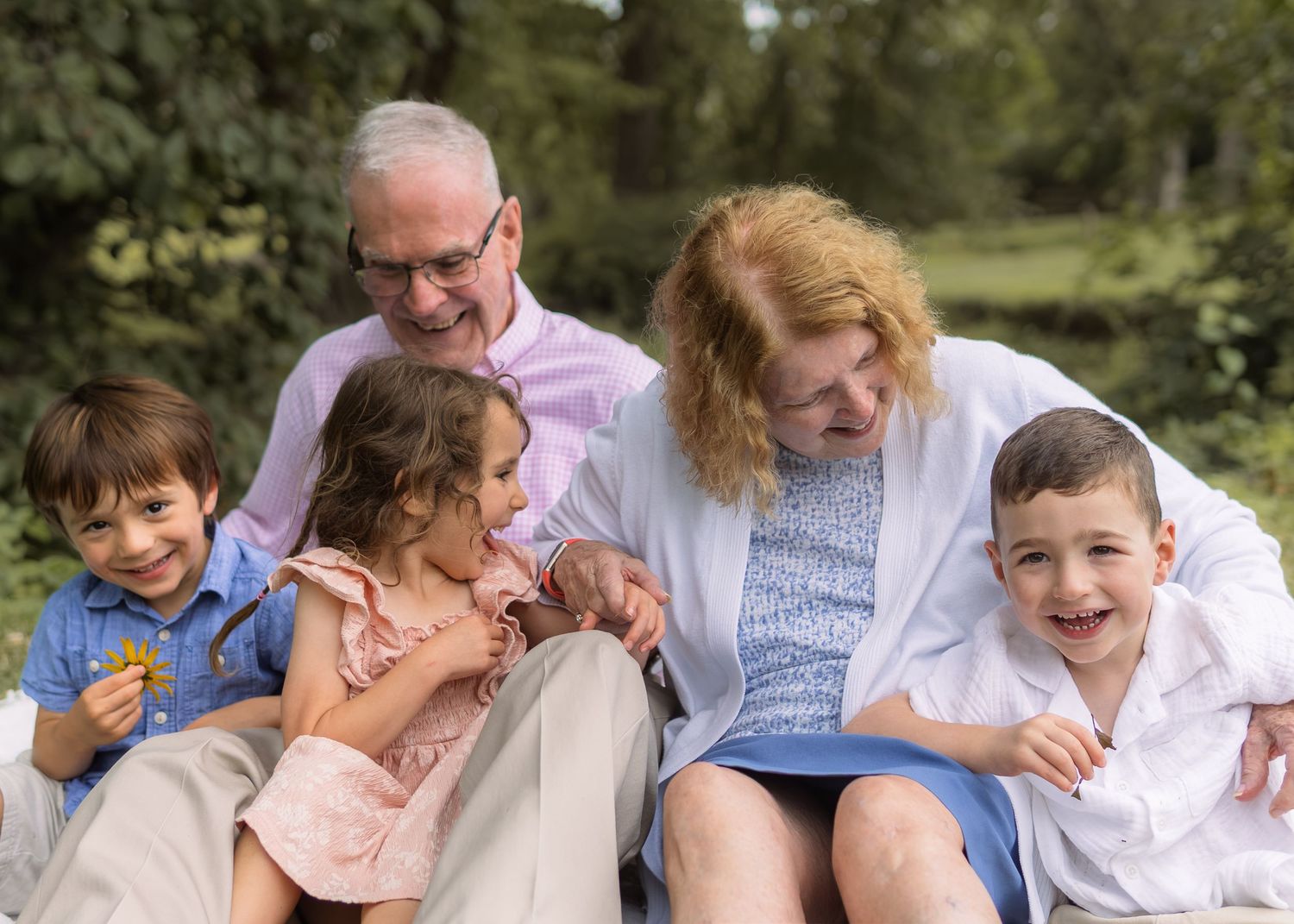Grandparents sit outdoors smiling with three young grandchildren during a warm family portrait session.