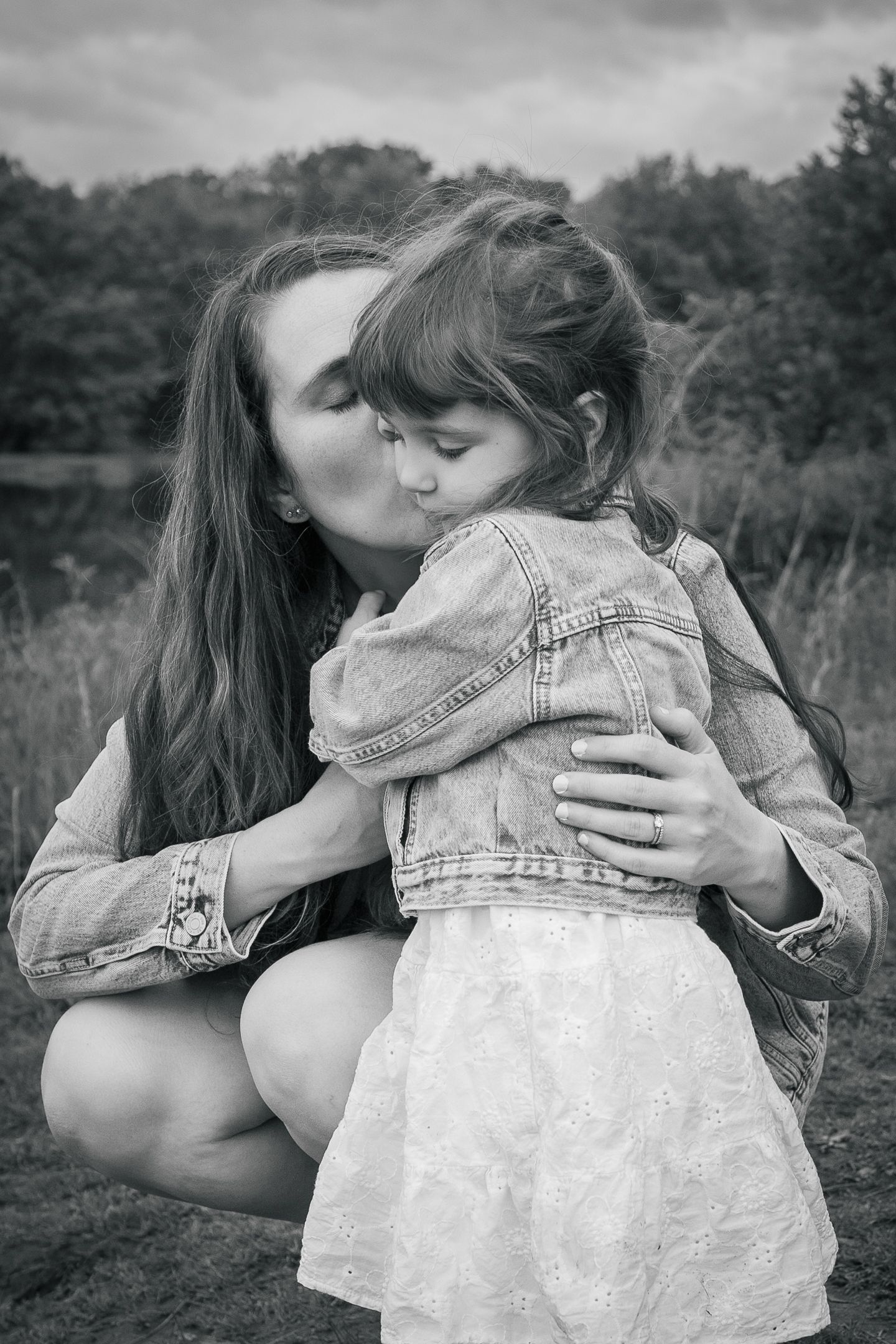 A tender black and white portrait of maternal affection shared outdoors amid a natural backdrop.
