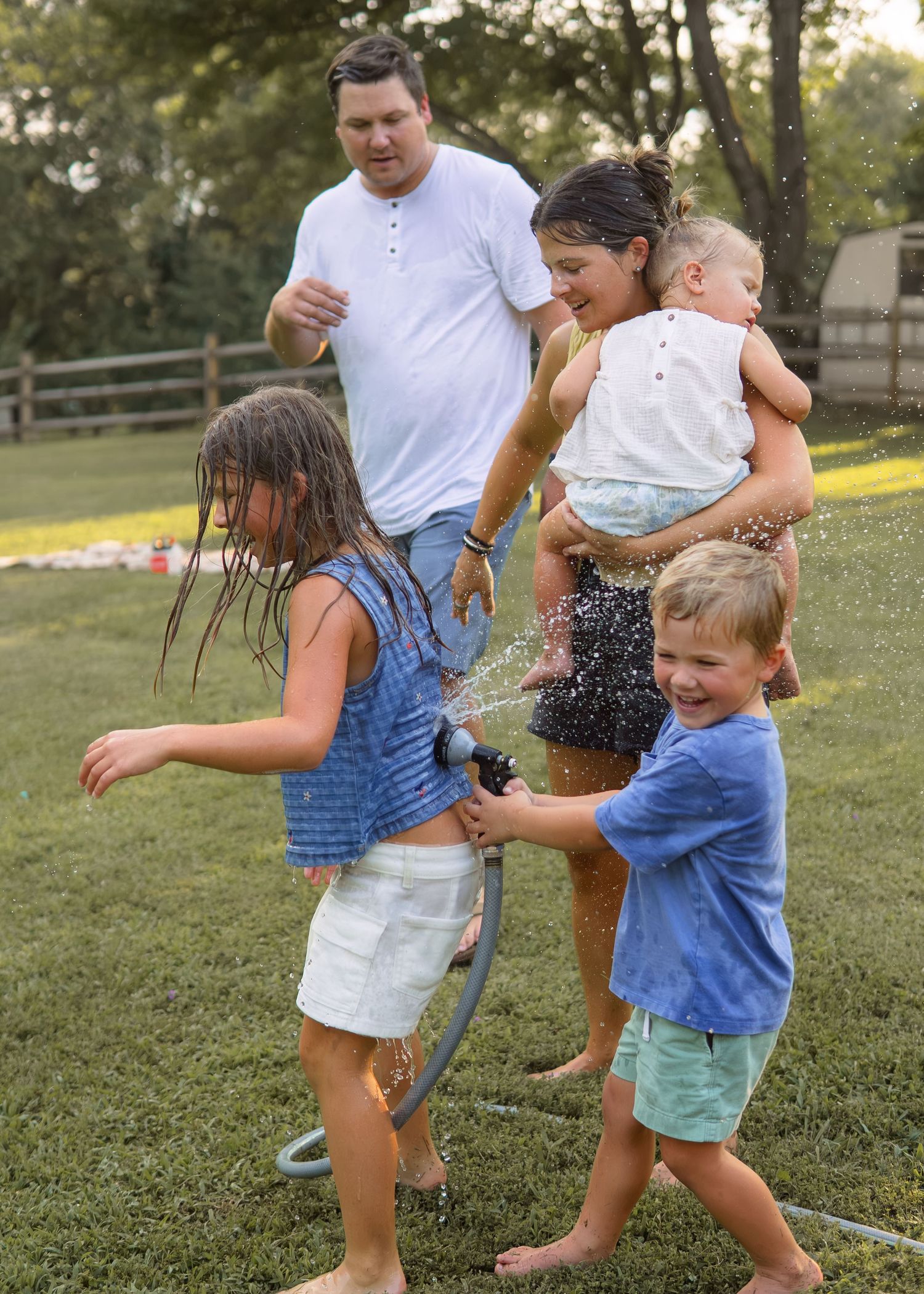 Family of five plays with garden hose in backyard, children getting soaked with water.