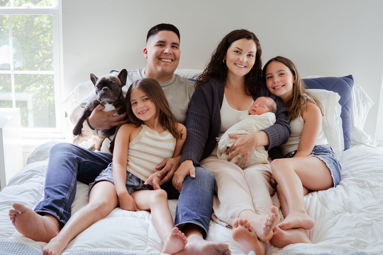 Happy family with small dog relaxing together on white bed at home.