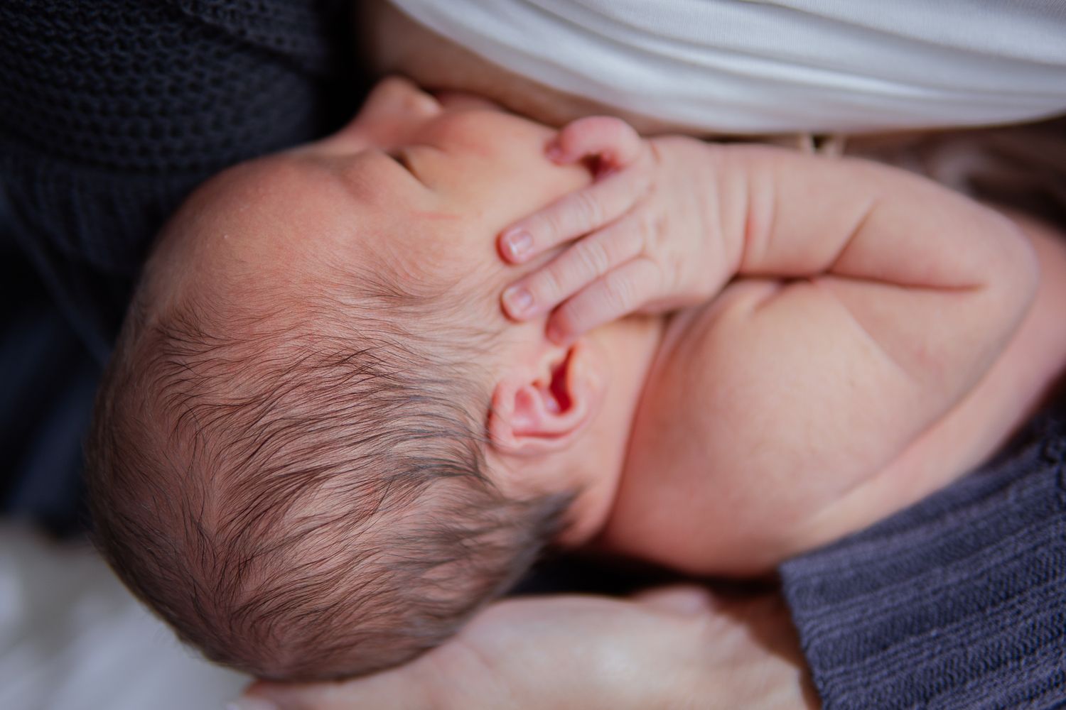 Close-up of sleeping newborn's head with delicate hand resting on blanket.