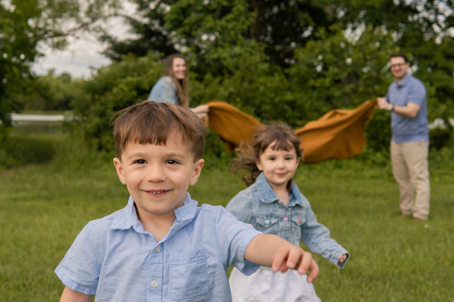 Young boy smiling in foreground with family playing on green grass in background.