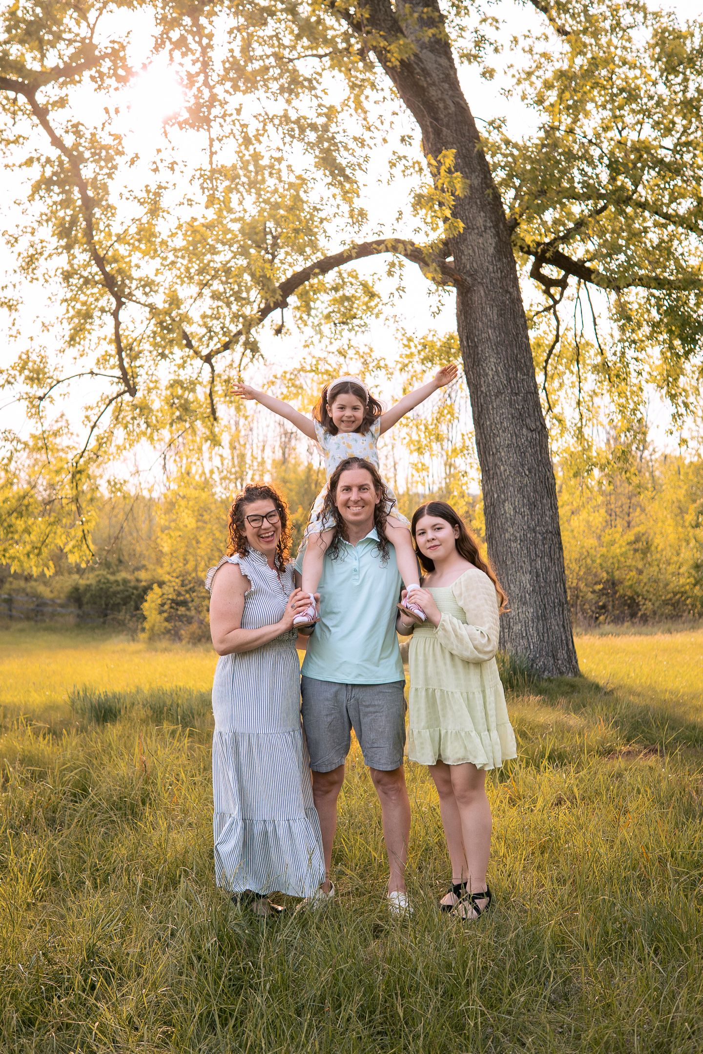 A family gathers under a large tree in a sunlit meadow with golden autumn foliage during a warm afternoon.