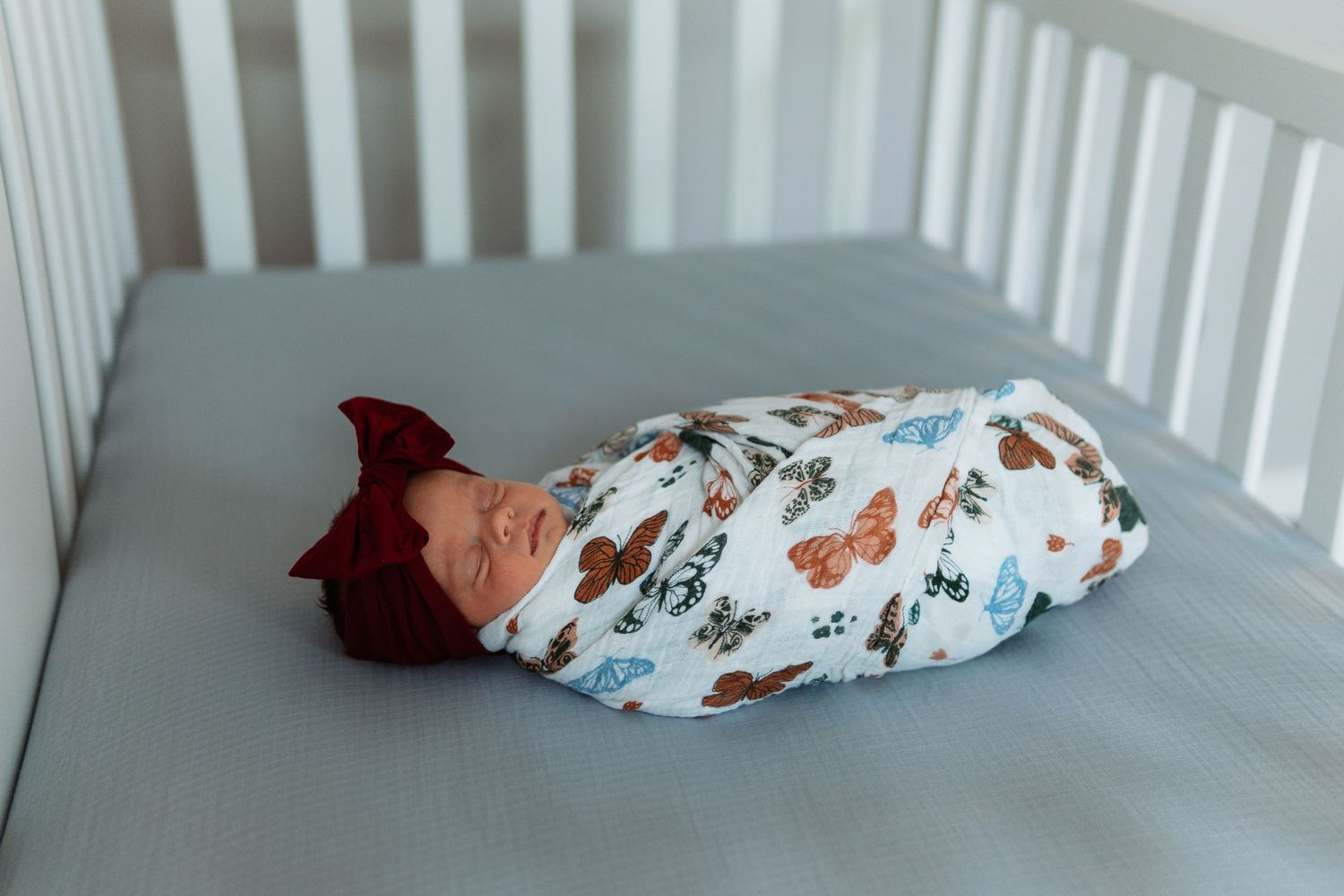 Baby crib with butterfly patterned swaddle blanket against white railing.