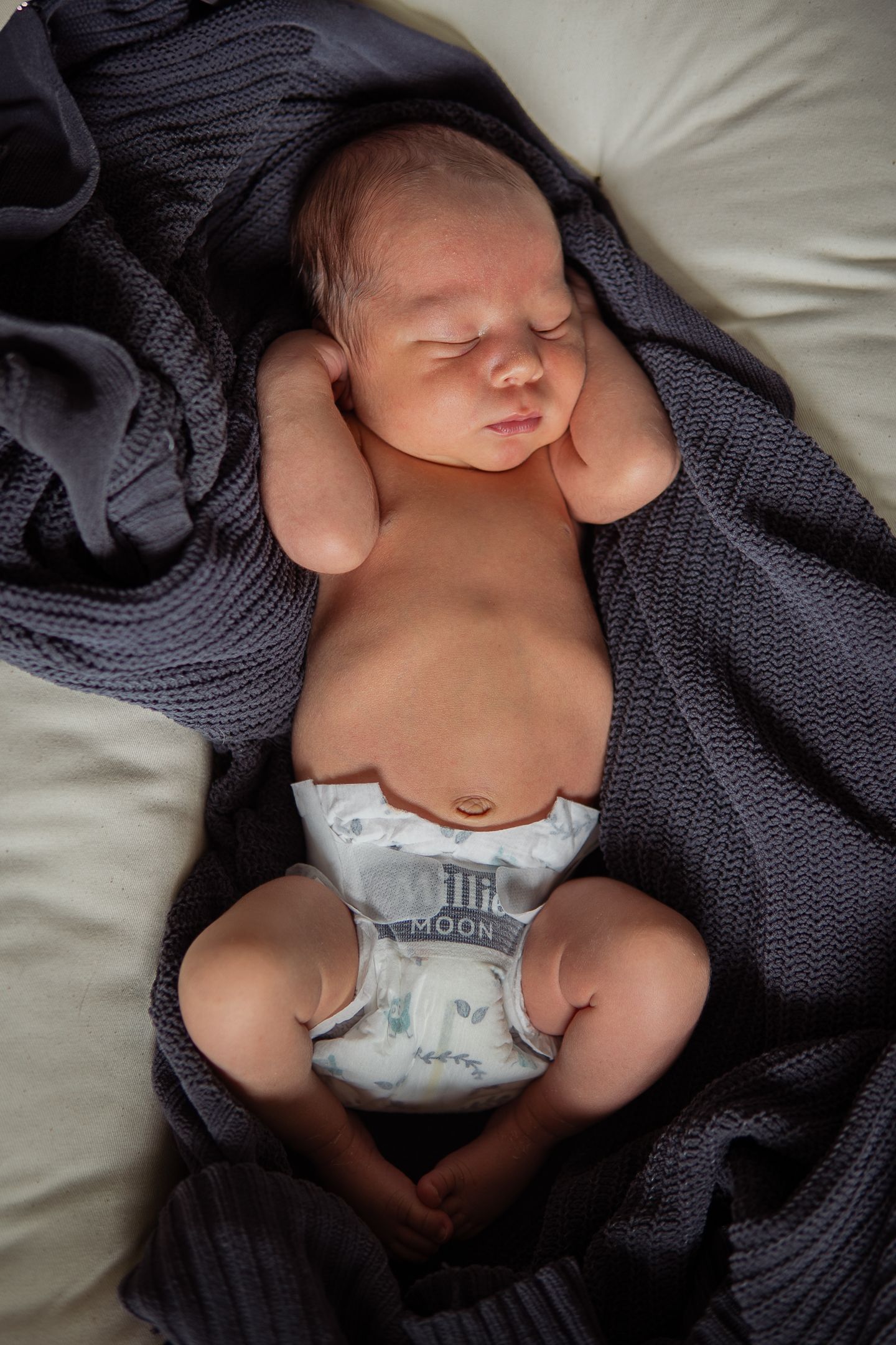 Sleeping newborn baby wearing diaper and wrapped in cozy navy knit blanket.