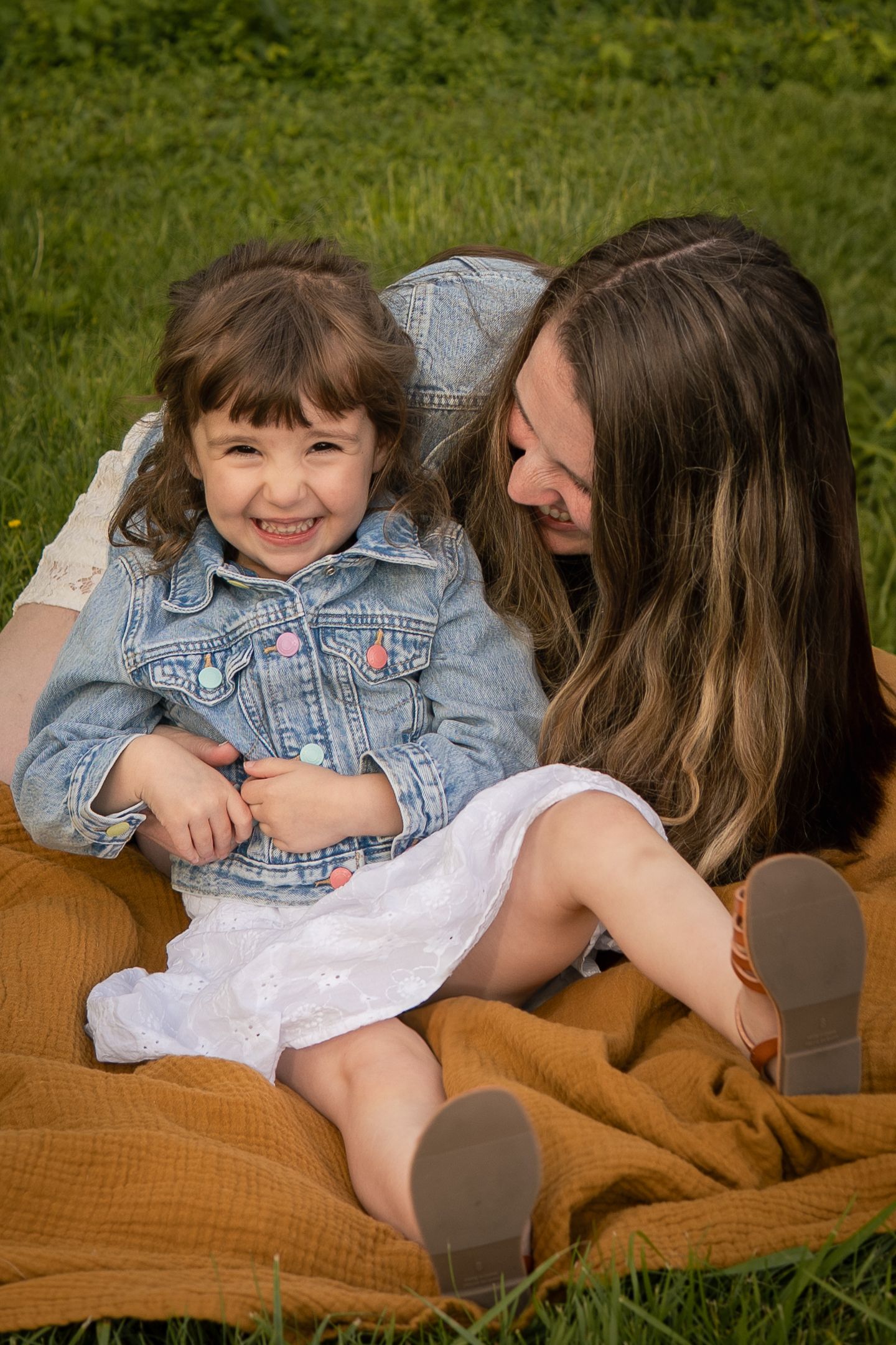 Two people share a joyful moment while sitting on a mustard yellow blanket in the grass on a sunny day.