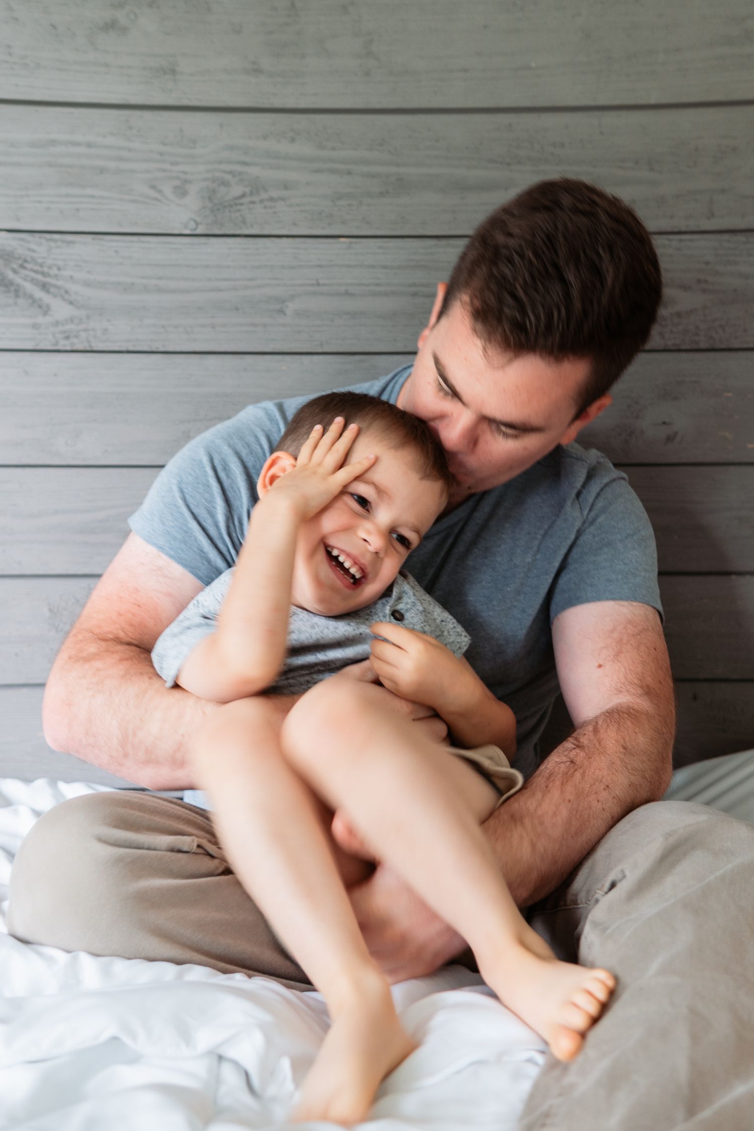 A tender playful moment between a parent and child laughing together against a rustic gray wood wall background.