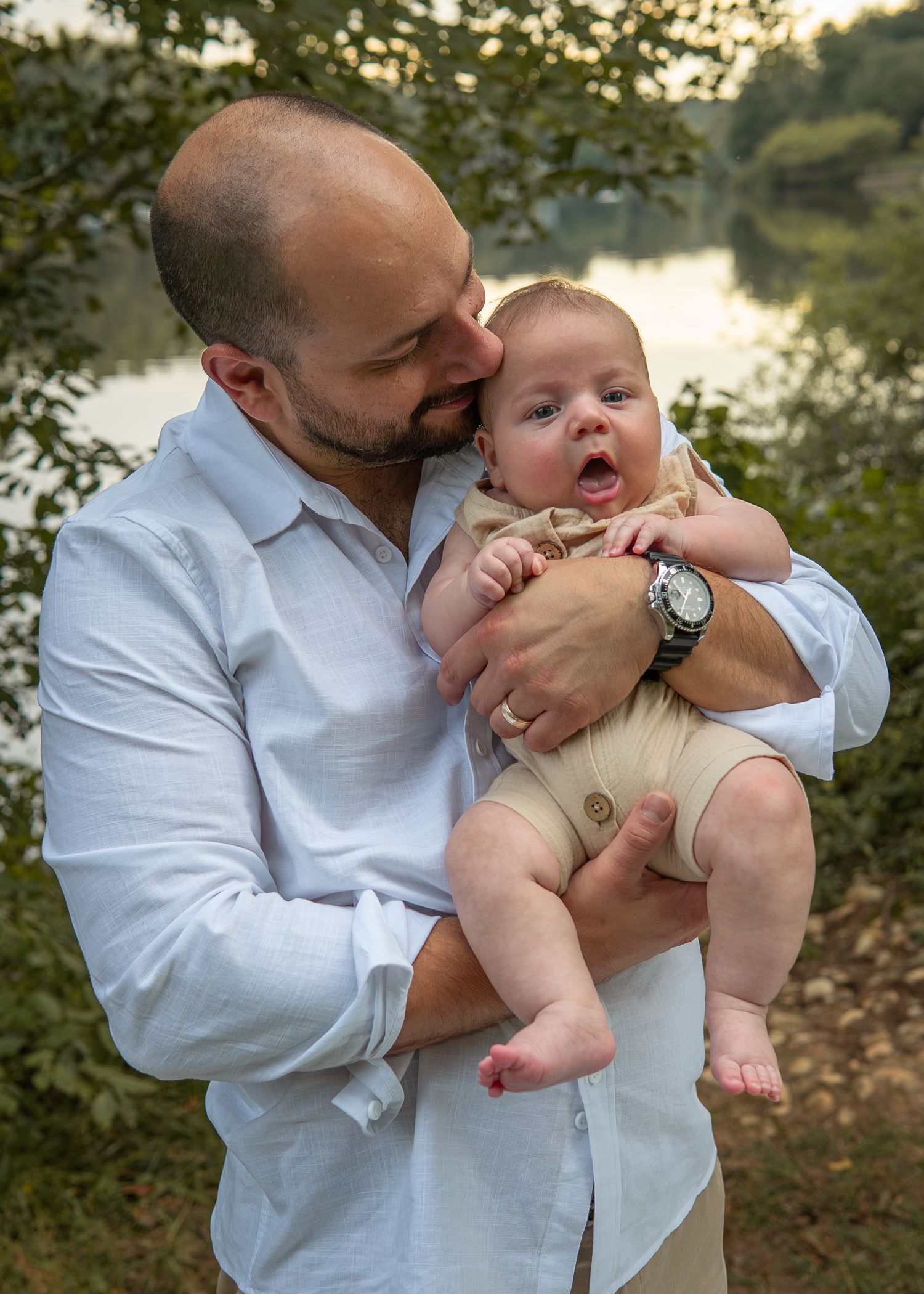 Loving father cradling his yawning newborn baby boy in his arms outdoors by a river.
