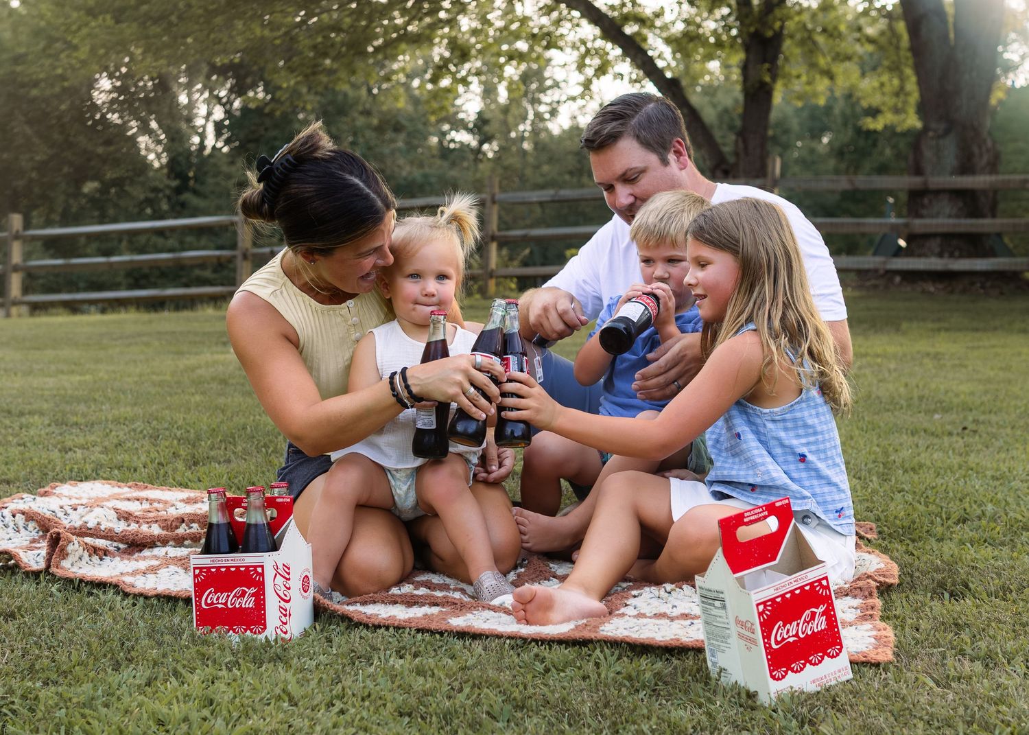 Family enjoying Coca-Cola drinks together on a blanket outdoors during a sunny picnic in a green park.