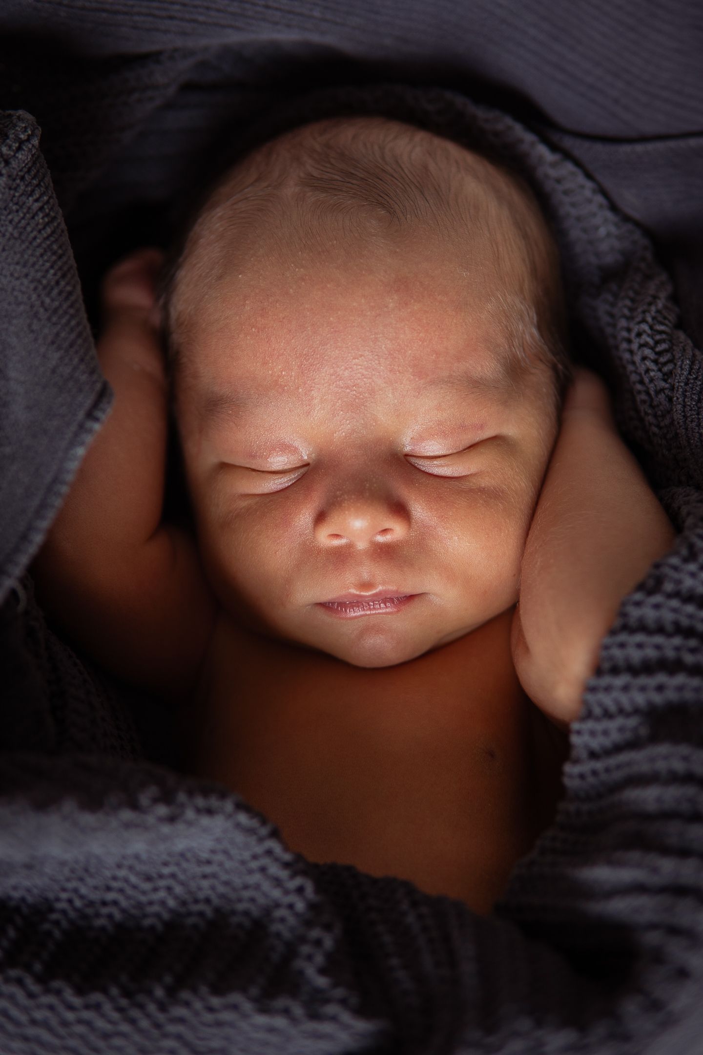 Sleeping newborn baby swaddled in dark gray knitted blanket in peaceful close-up portrait.