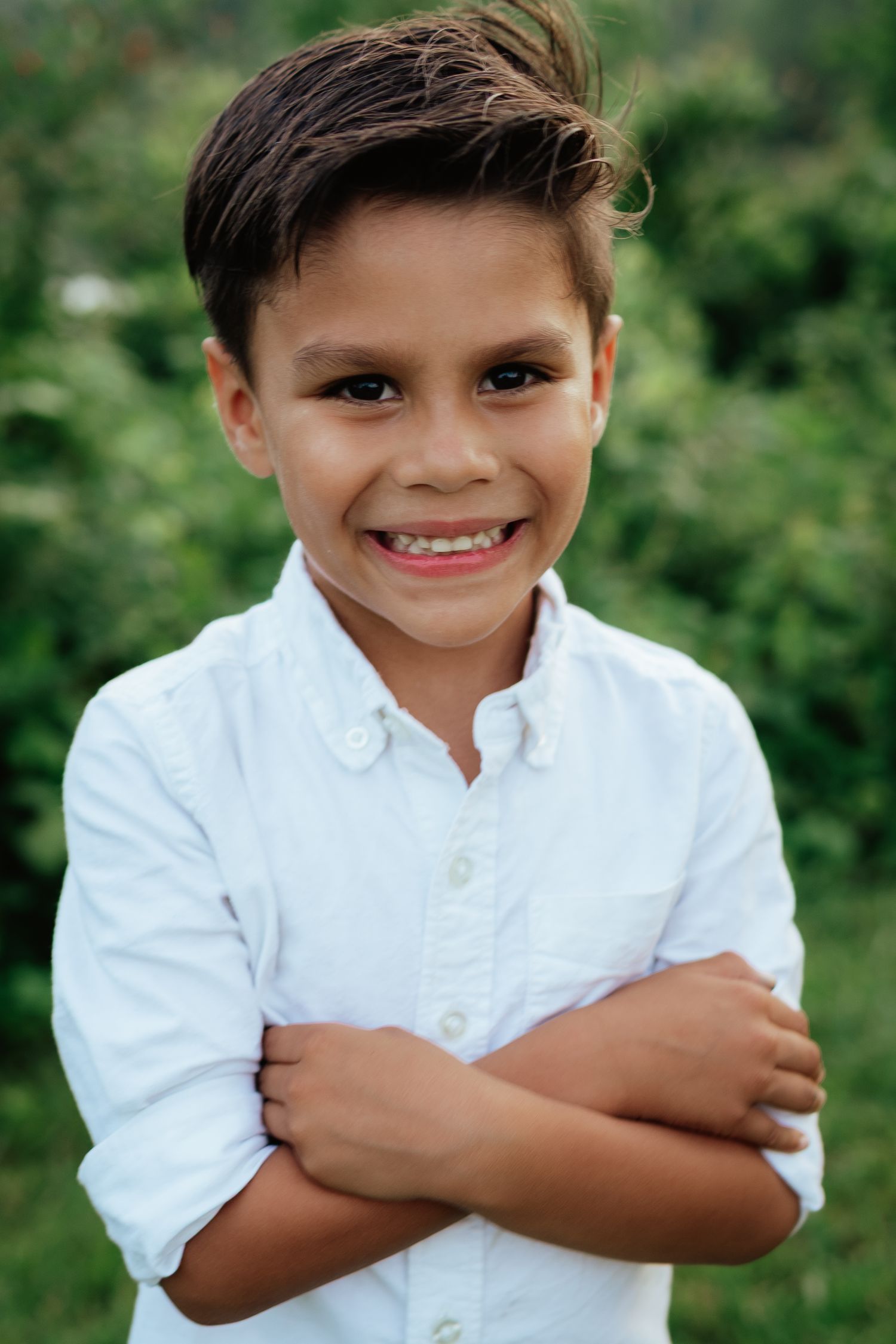 Young person in white button-down shirt smiling confidently against green foliage.