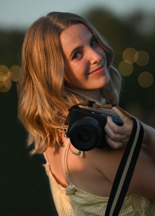 Young woman holding a camera outdoors in warm golden bokeh light.