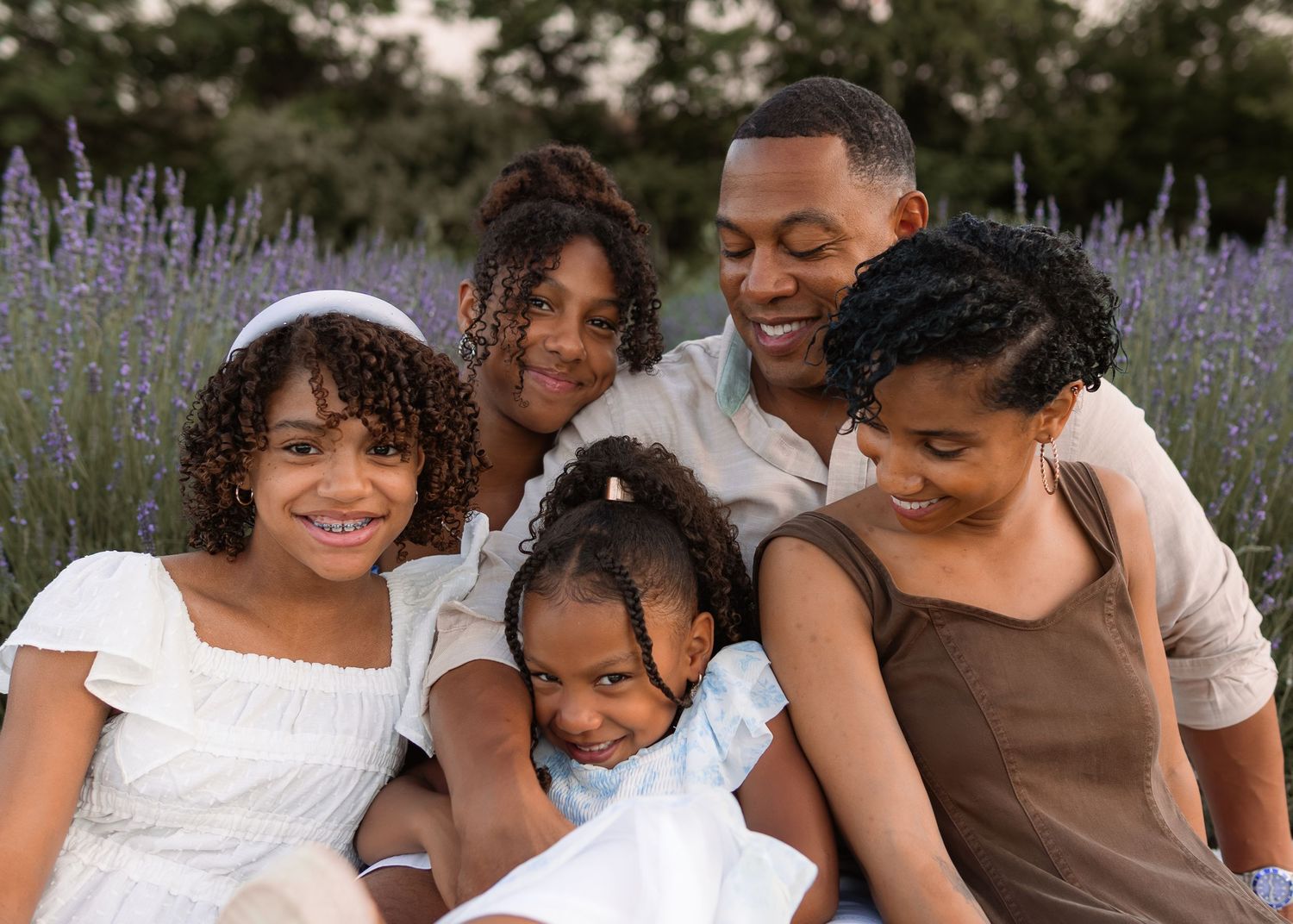A joyful Black family of five sitting together in a blooming lavender field during golden hour.