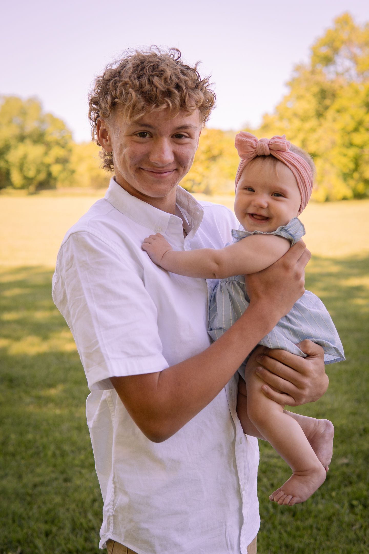 A sweet outdoor portrait showing a tender moment between a teenager and baby in a park setting at golden hour.