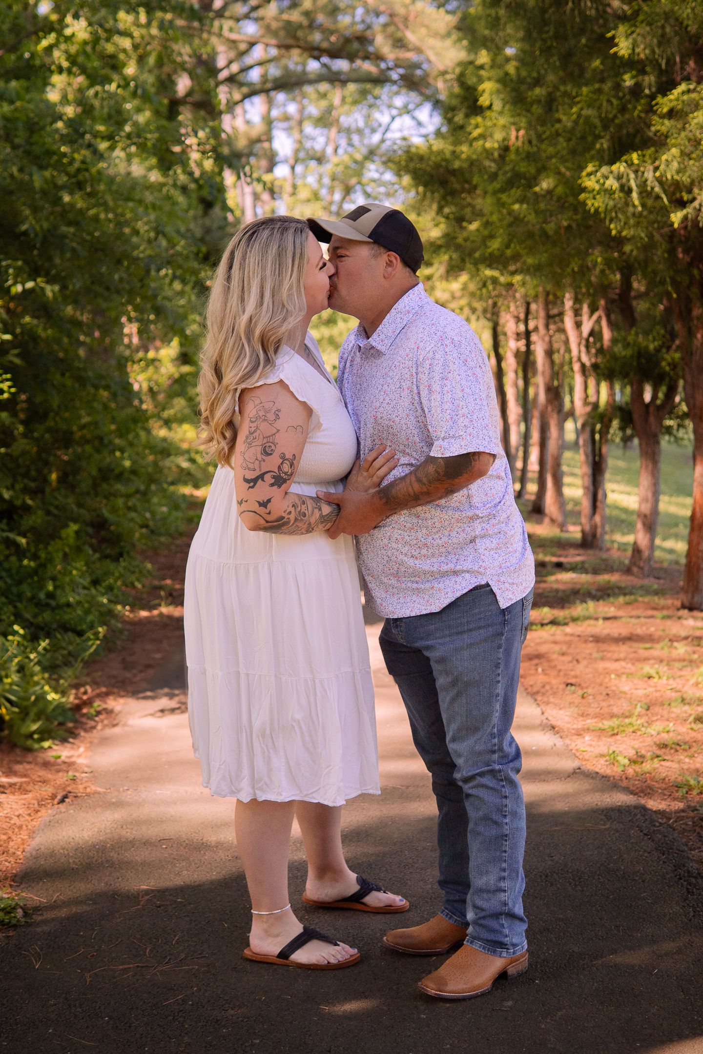 A romantic couple sharing a kiss on a tree-lined path during golden hour.