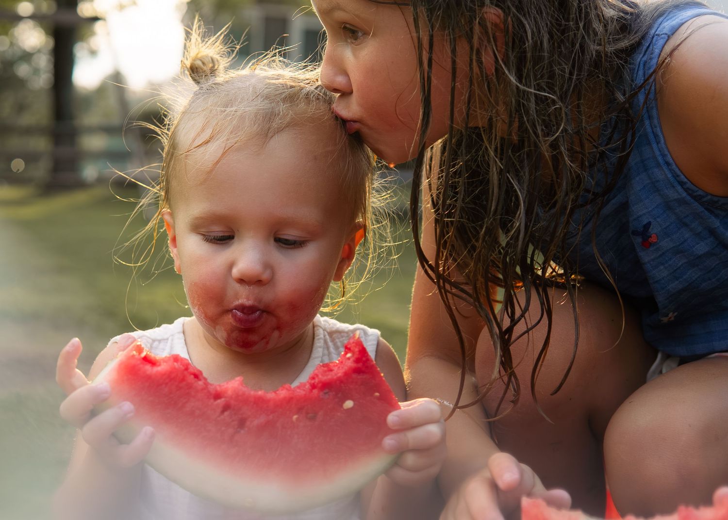 Two young sisters share a large slice of juicy watermelon together outdoors on a sunny day.