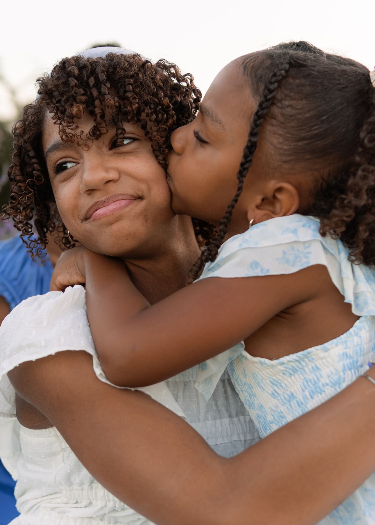 A young girl gives an affectionate kiss on the cheek to her smiling older sister during a family photo session.