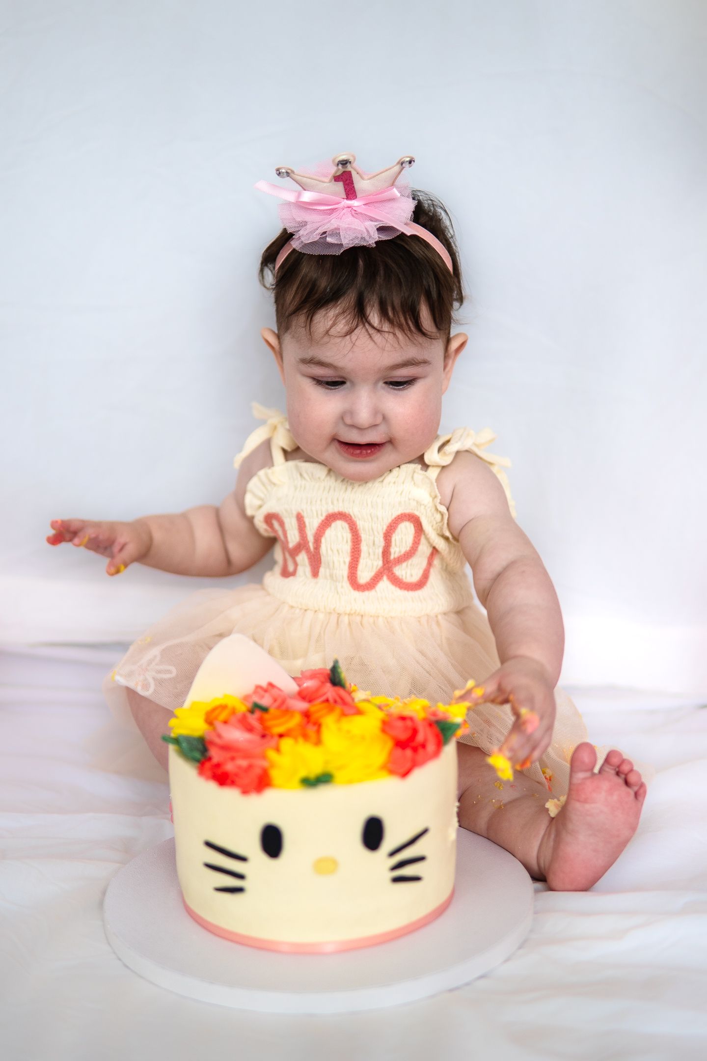 A Hello Kitty themed birthday cake with colorful toppings next to a cream tulle dress.