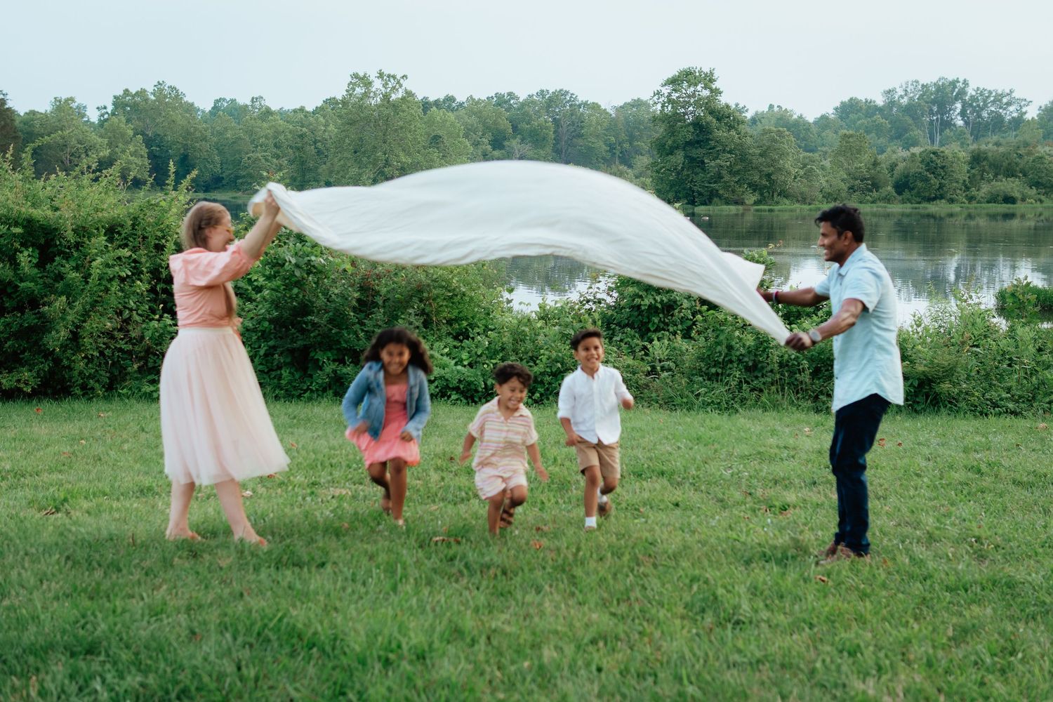 A group plays with flowing white fabric in a grassy field on a cloudy day.