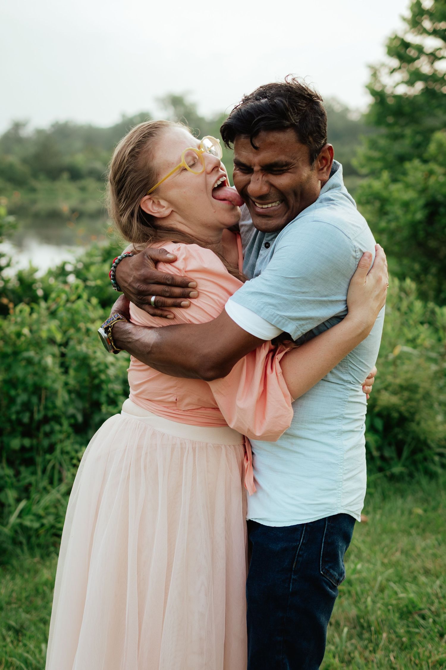 A couple shares romantic kisses and embraces in a green outdoor setting wearing pink and light blue outfits.
