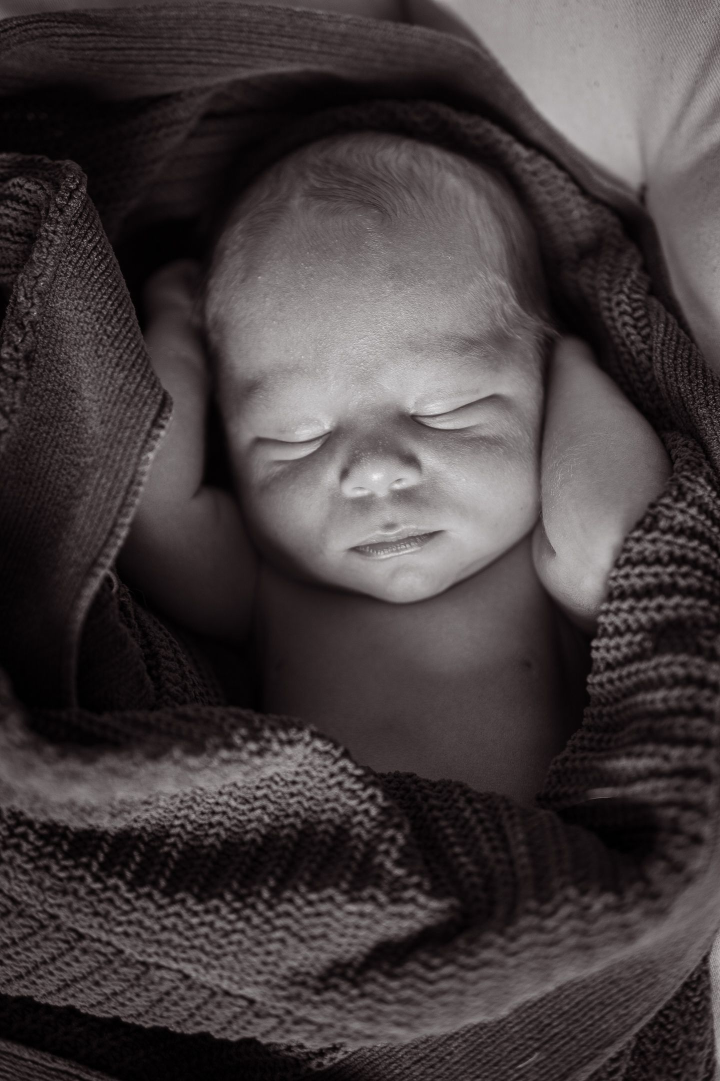 Black and white photos of a sleeping newborn swaddled in a soft knitted blanket.