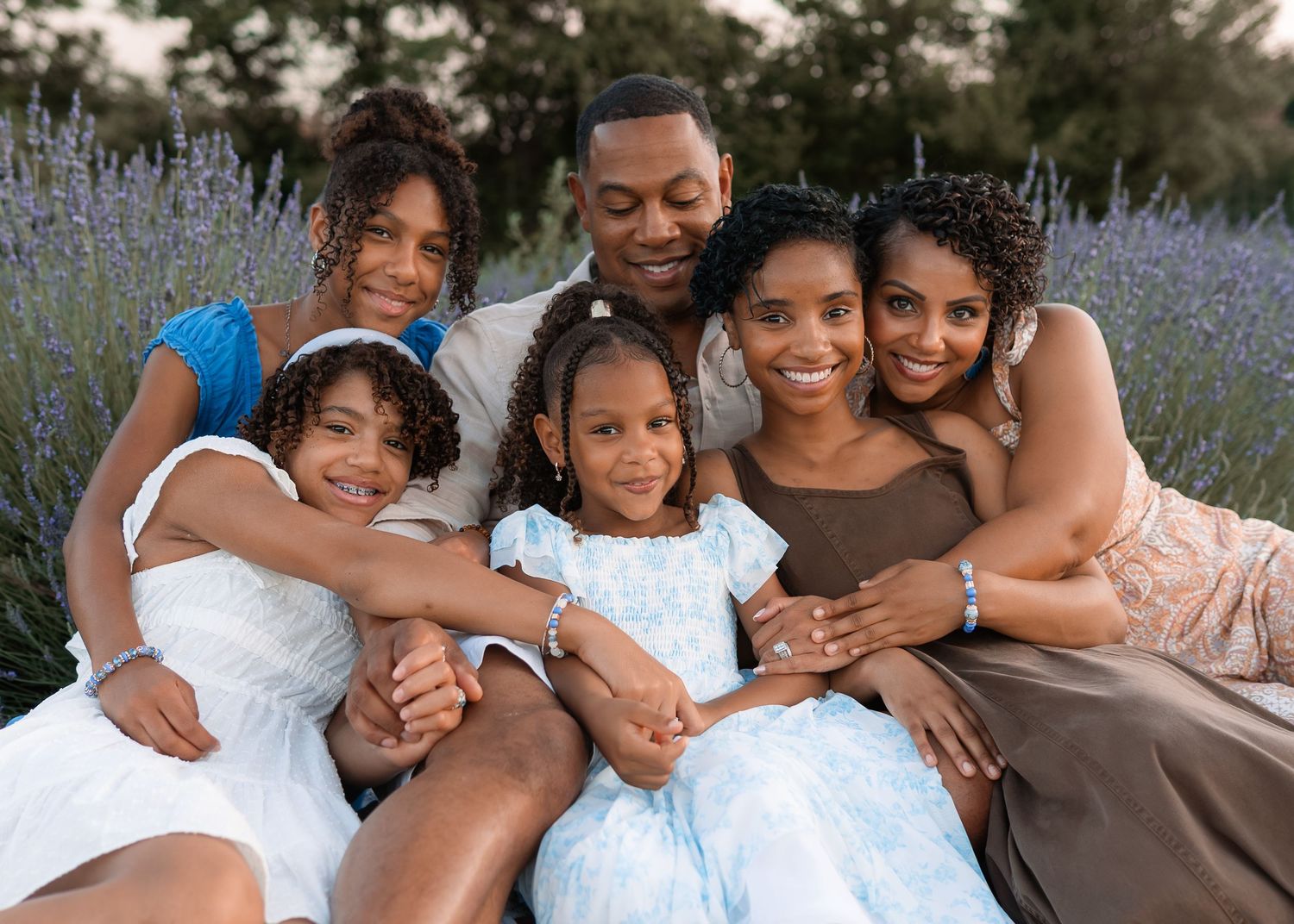 Happy family of six posing together in a lavender field during golden hour, smiling warmly at the camera.