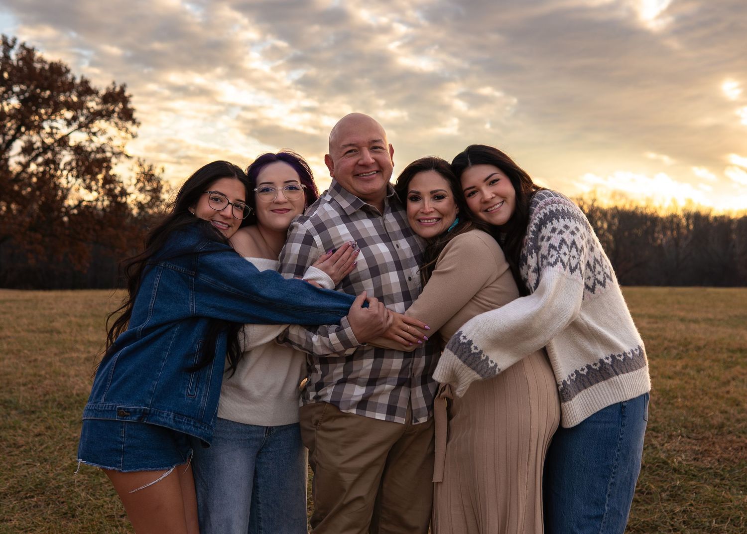 Happy family of five hugging together in a field during a beautiful autumn sunset.