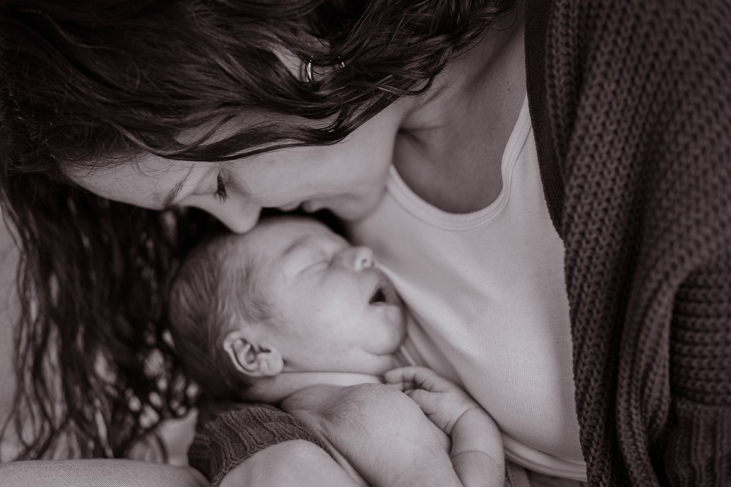 Intimate black and white portrait of parent tenderly kissing sleeping newborn.